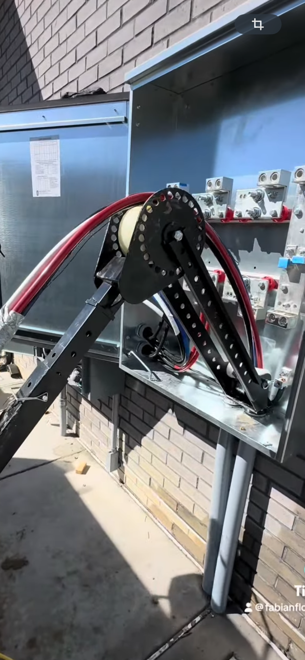 Electrical cables being installed in an enclosure using a cable bender on a brick building exterior.