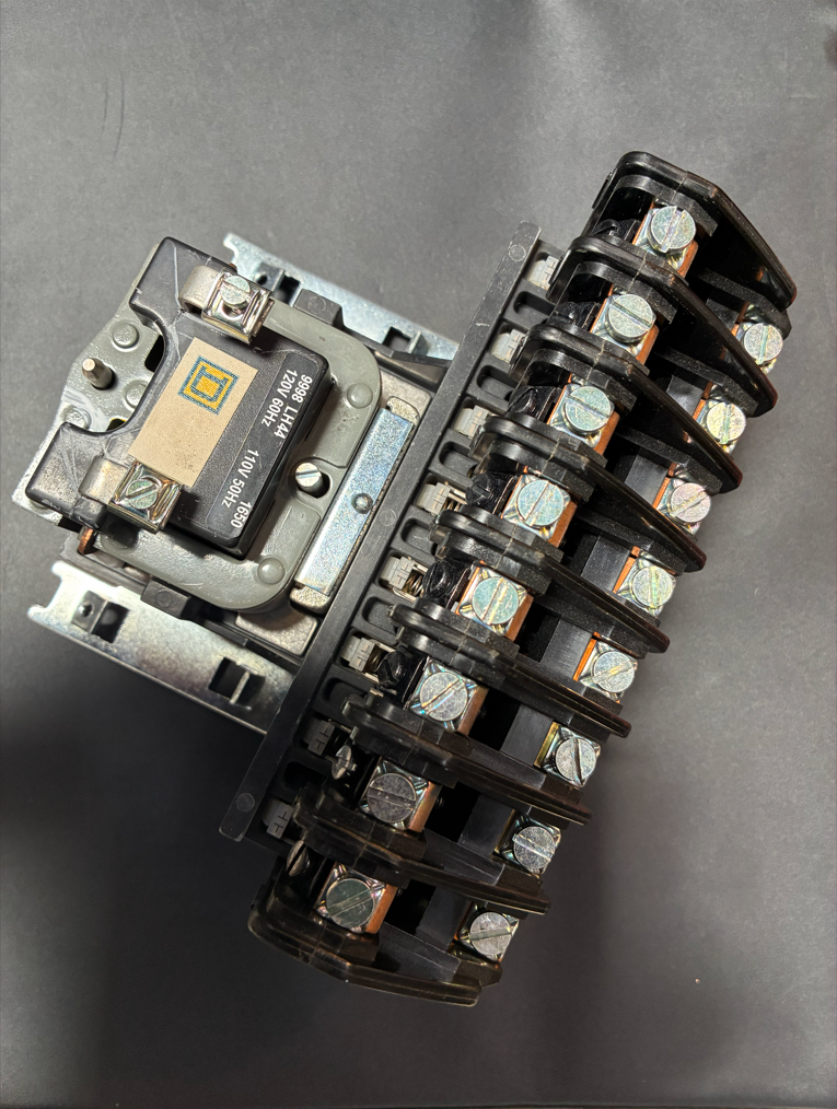 Electrical contactor with black plastic and silver metal components on a dark background.