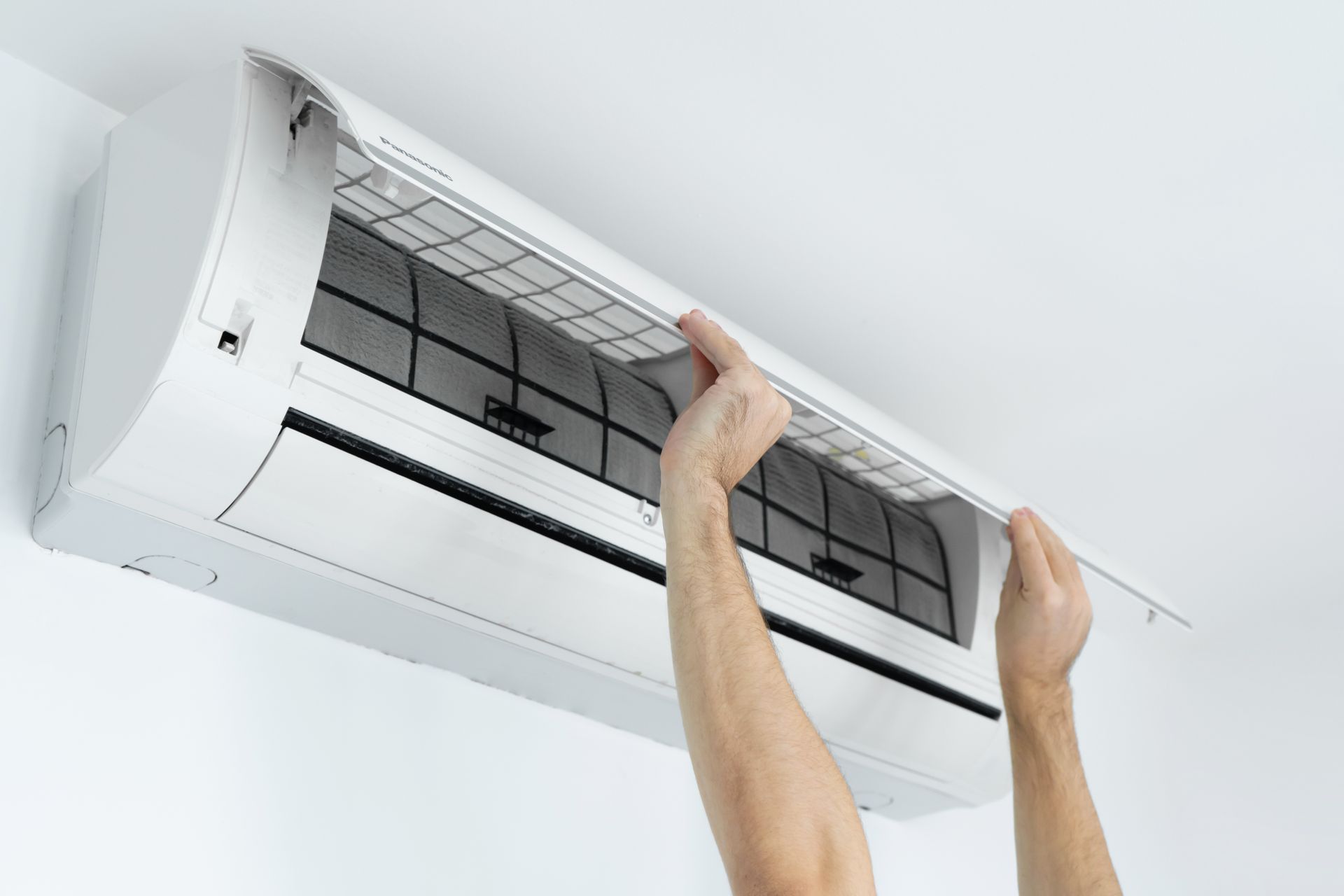 Hands installing a white wall-mounted air conditioner ceiling unit Hands installing a white wall-mounted air conditioner ceiling unit