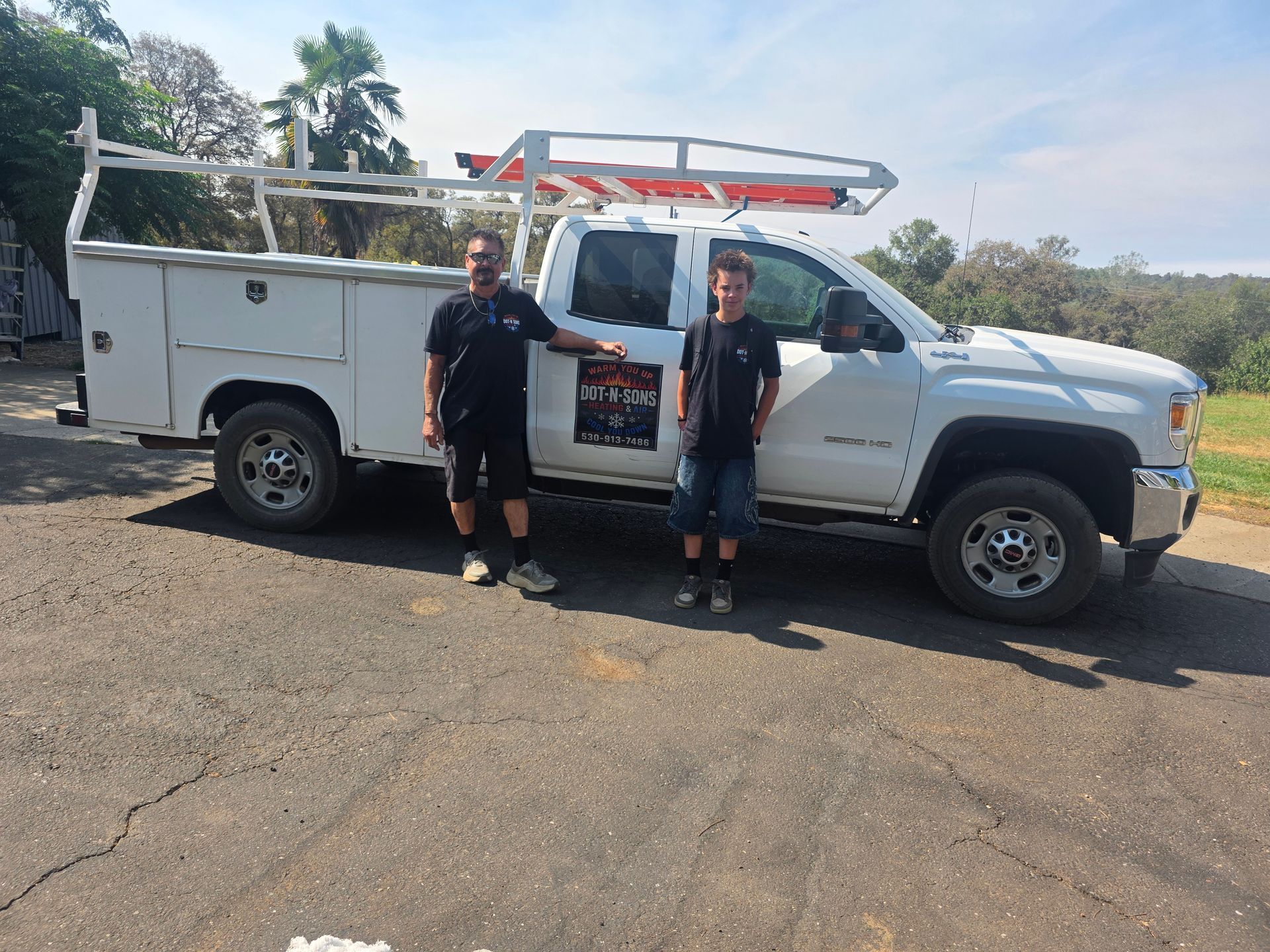 Two people standing beside a white utility truck parked on a sunny roadside. Two people standing beside a white utility truck parked on a sunny roadside.