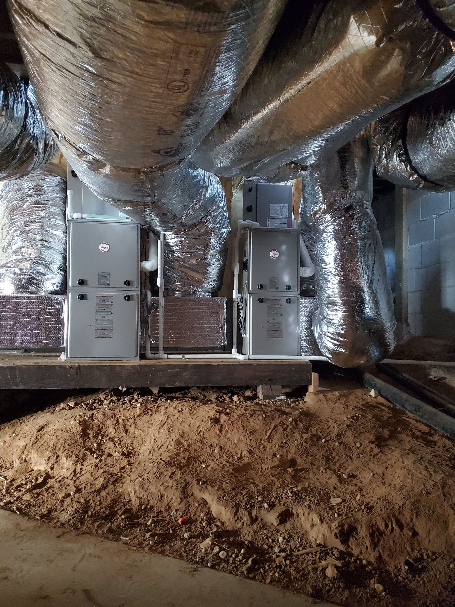 Attic with foil-wrapped ducts and two metal HVAC units above insulation debris