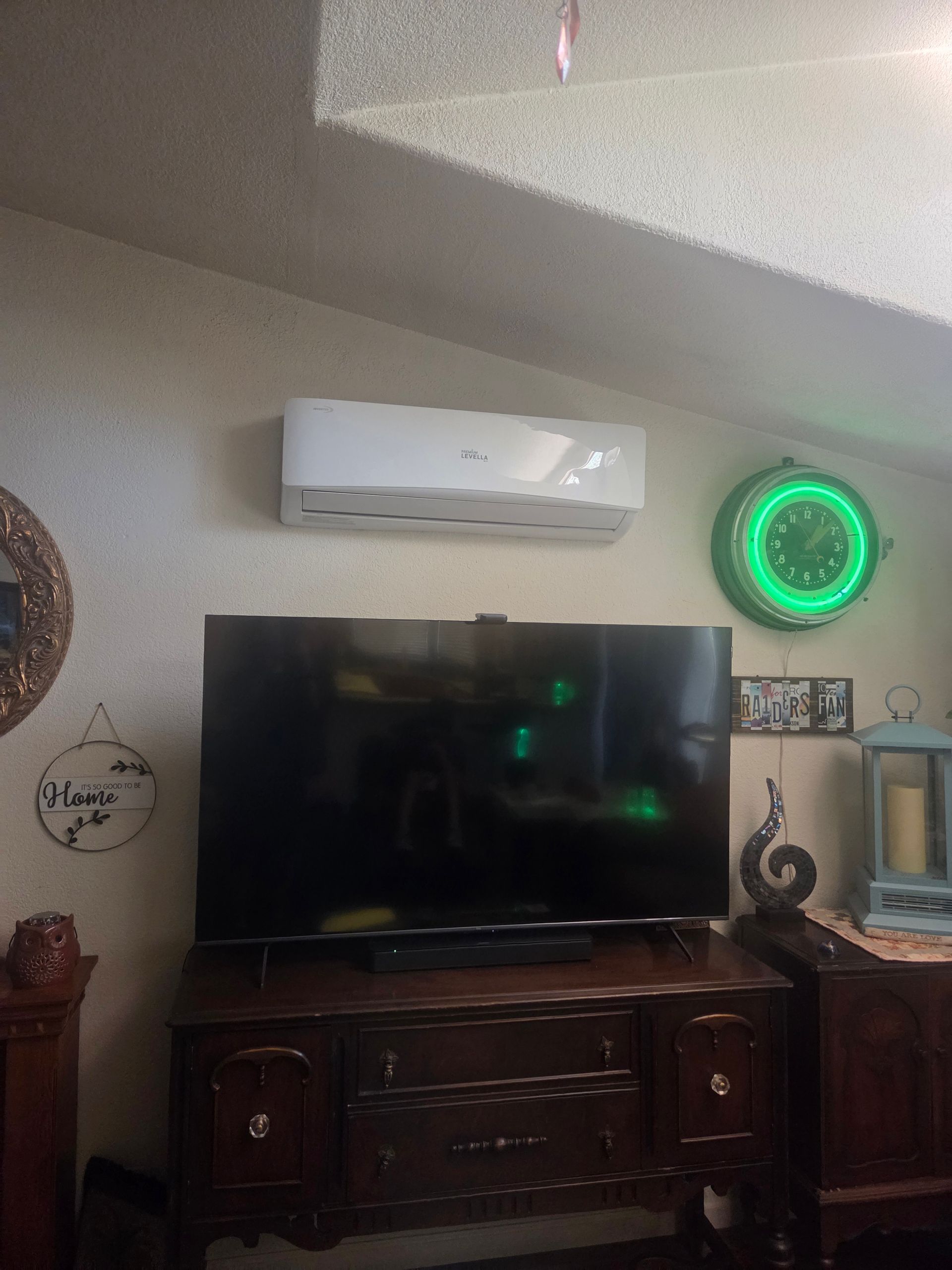 Living room wall with a TV, air conditioner, and green neon clock above a wooden cabinet Living room wall with a TV, air conditioner, and green neon clock above a wooden cabinet