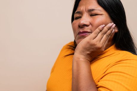 Woman with hand on cheek, grimacing, possible toothache.