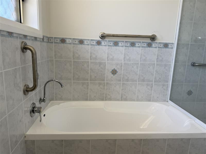 Bathroom with a white bathtub, gray tiled walls, and grab bars. - A1 Maintenance and Building In Old Bar, NSW