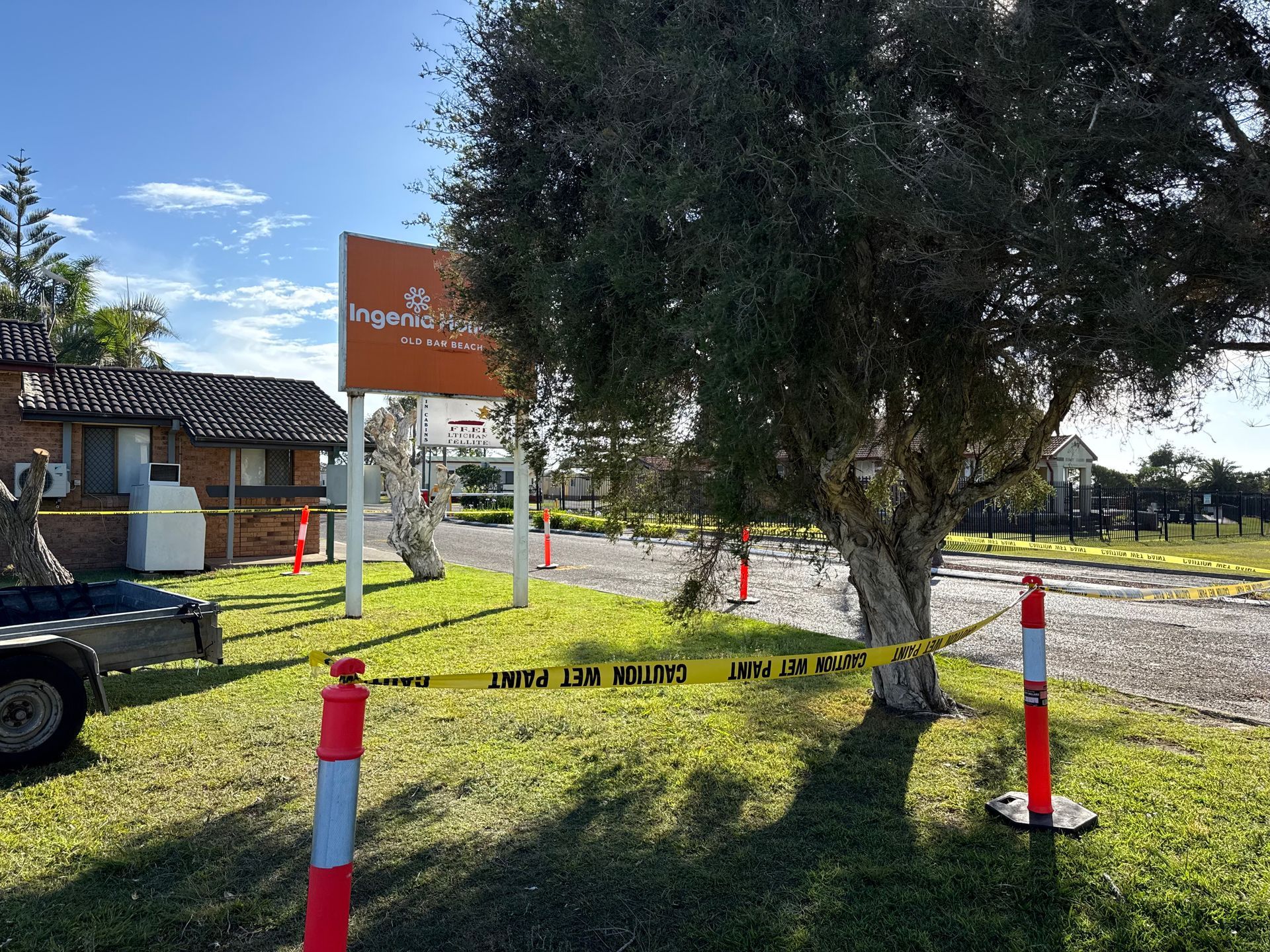 Exterior view of motel with caution tape. Sign, trees, brick buildings, and trailer visible under a sunny sky. - A1 Maintenance and Building In Old Bar, NSW