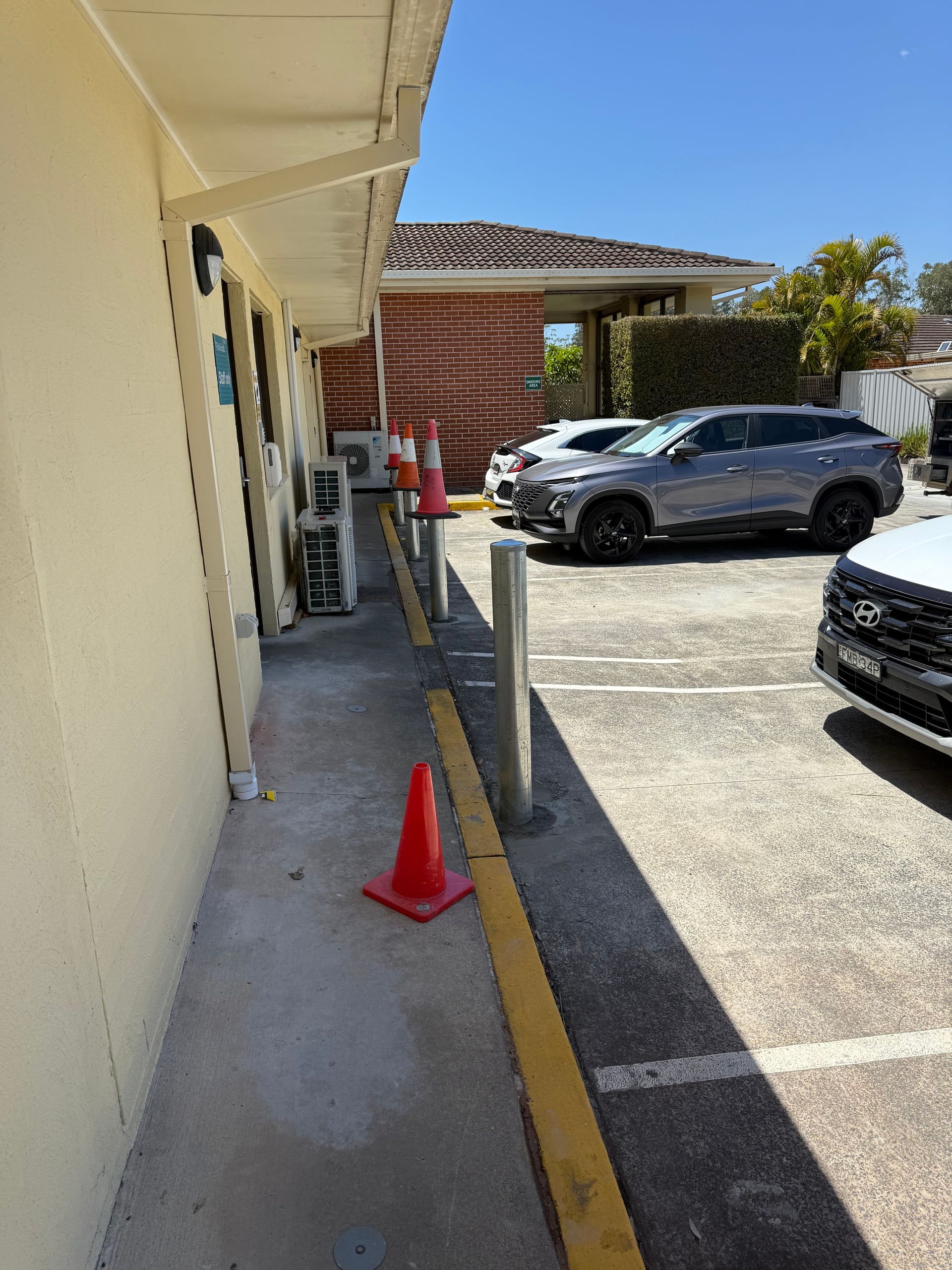 Exterior view of building with parked cars. Orange cones line the sidewalk next to a yellow curb - A1 Maintenance and Building, NSW
