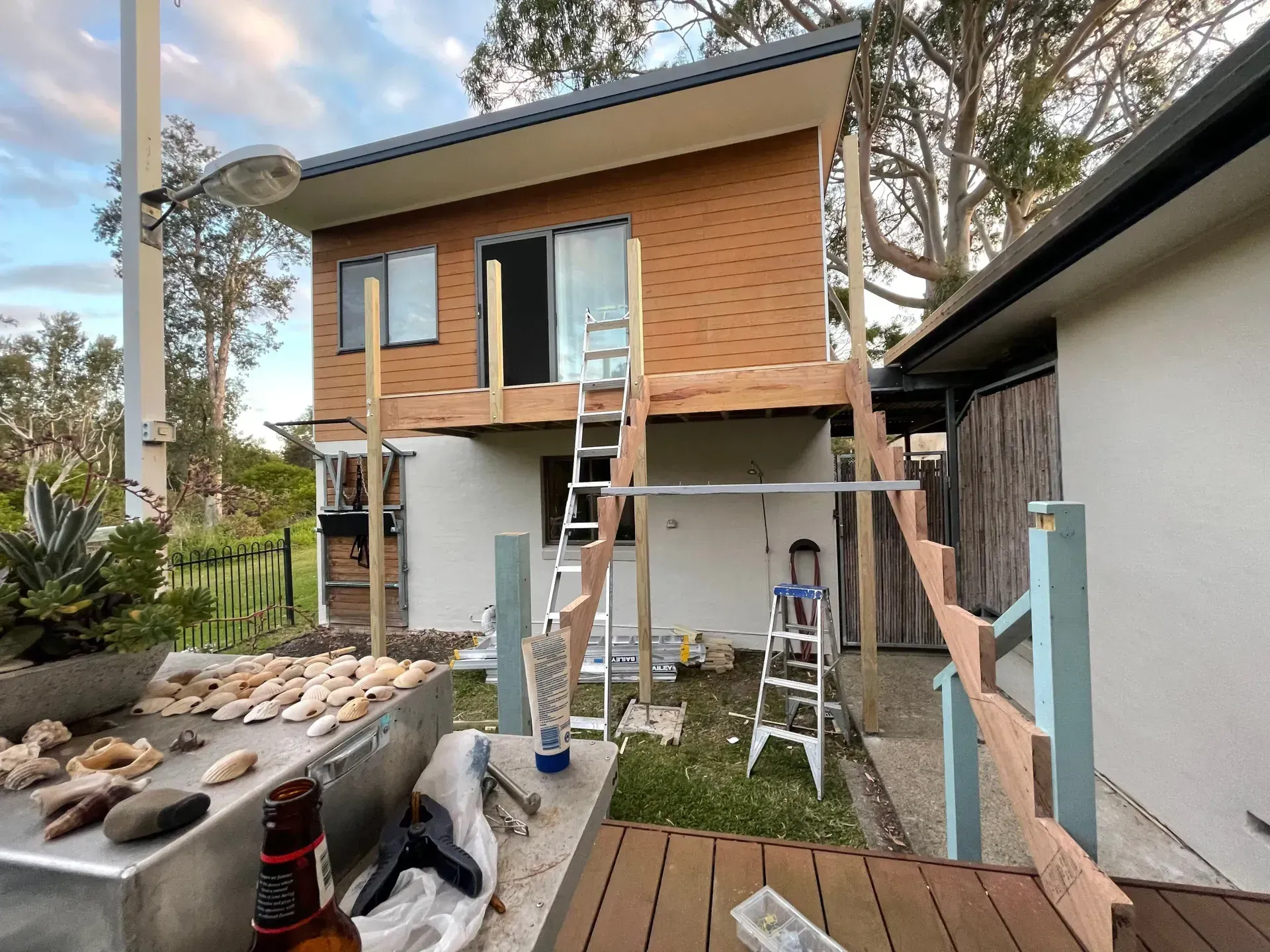 House under construction, with wood deck and ladder, surrounded by trees and a garden. - A1 Maintenance and Building In Old Bar, NSW