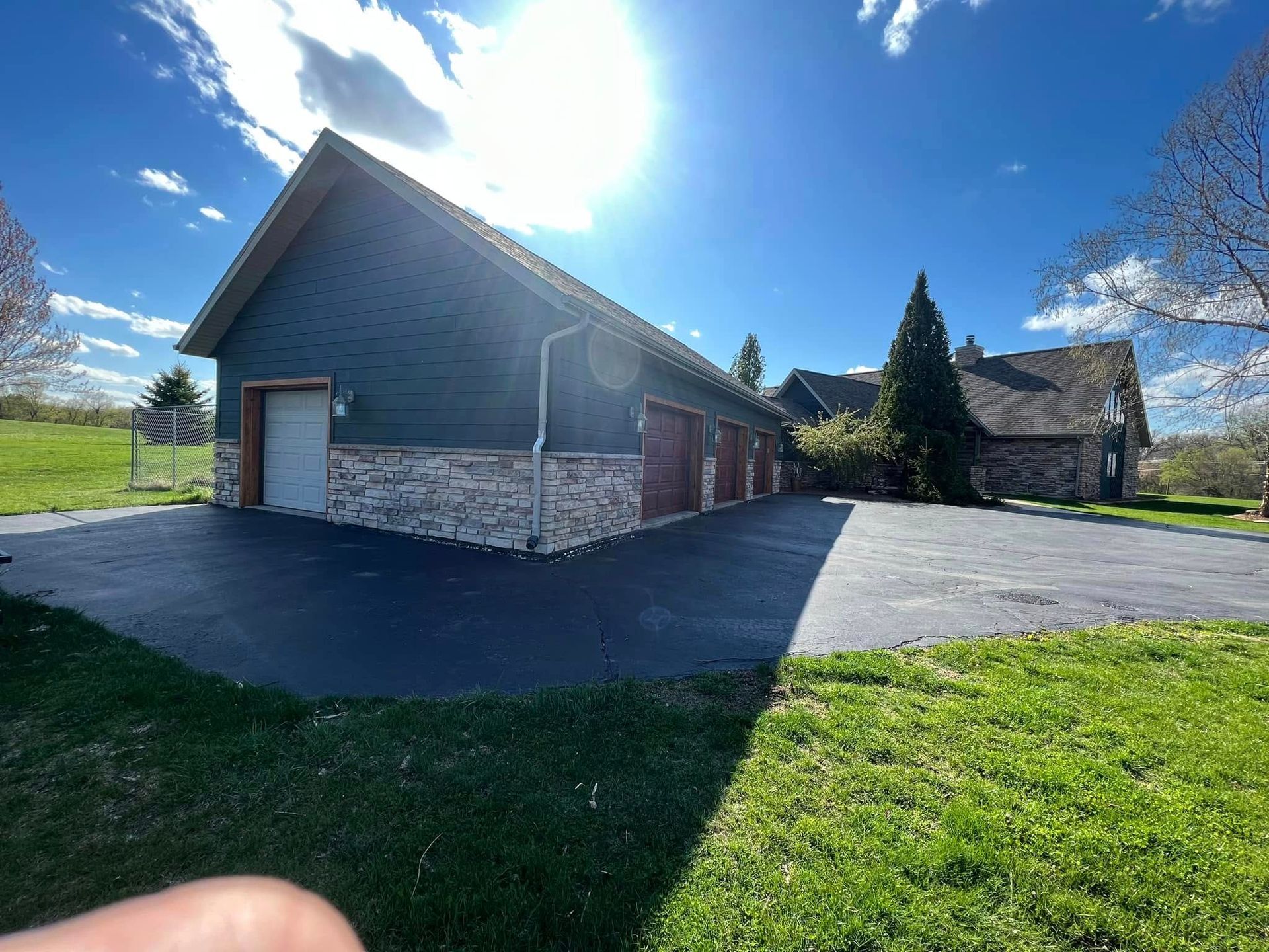 A long, green garage with stone accents and multiple red doors sits on a blacktop driveway on a sunny day.