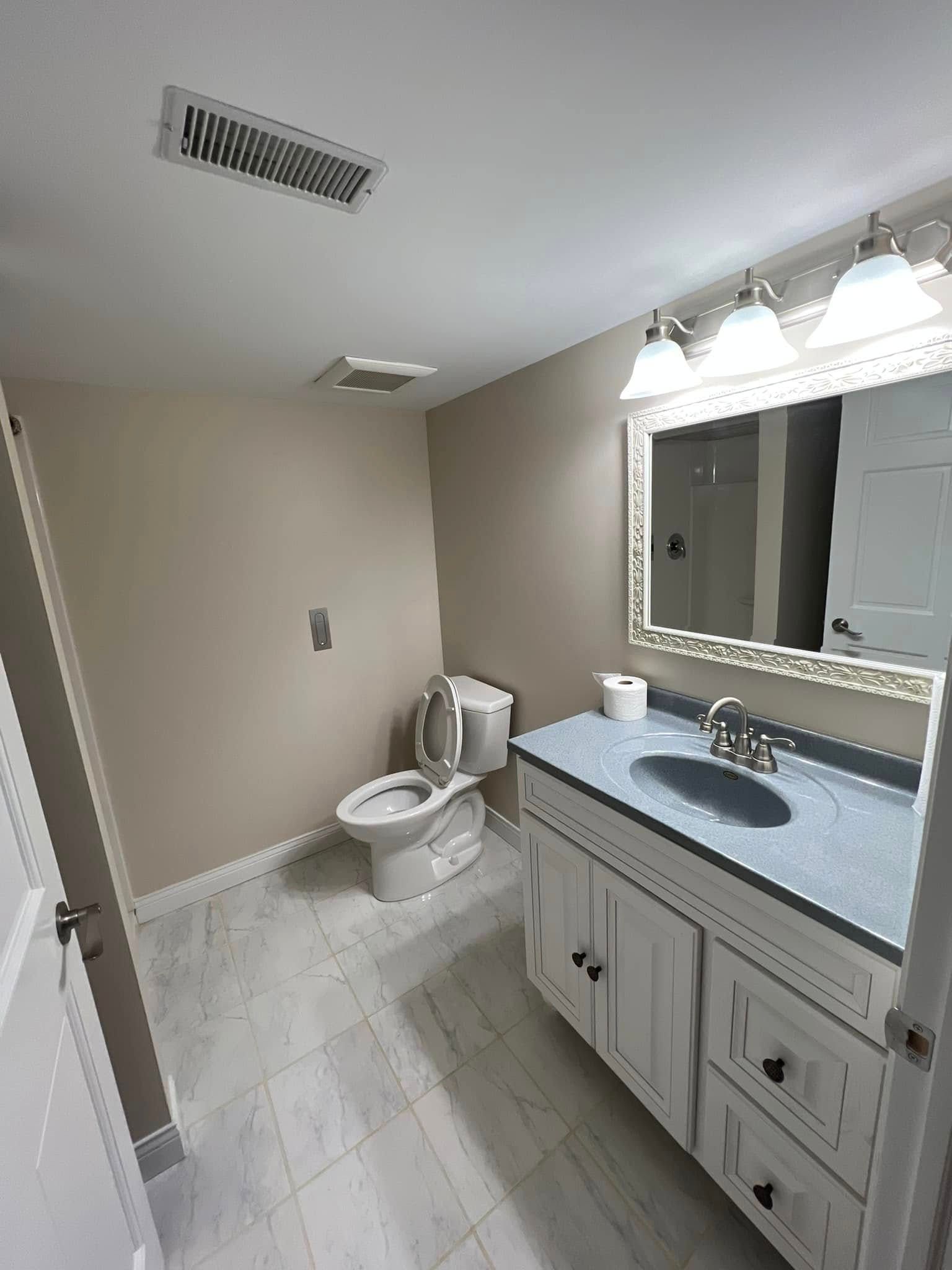 Bathroom with toilet, vanity, and mirror, featuring beige walls and white trim.