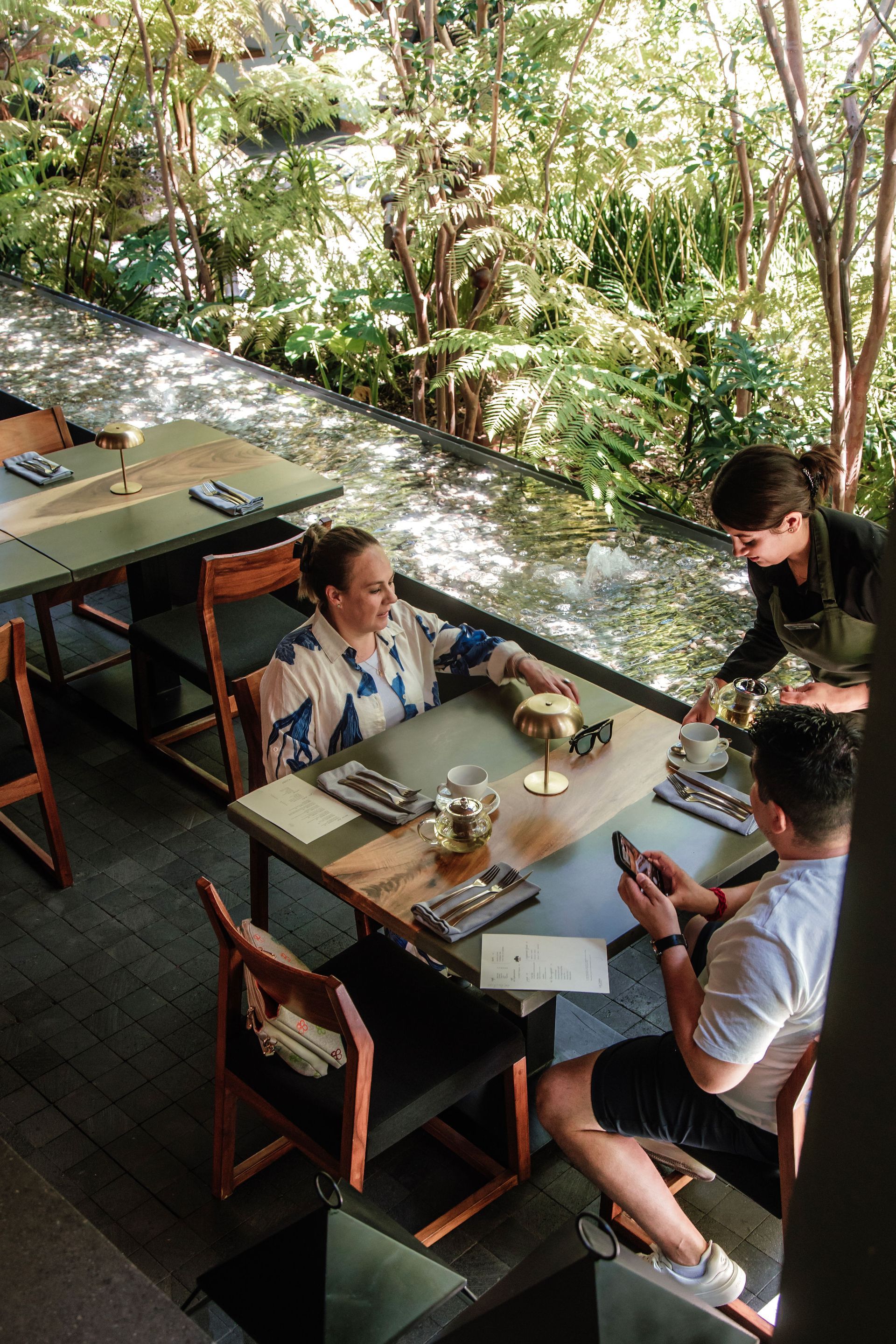 Tres personas compartiendo una comida en la terraza del restaurante La Casa Rodavento en su terraza junto al espejo de agua.