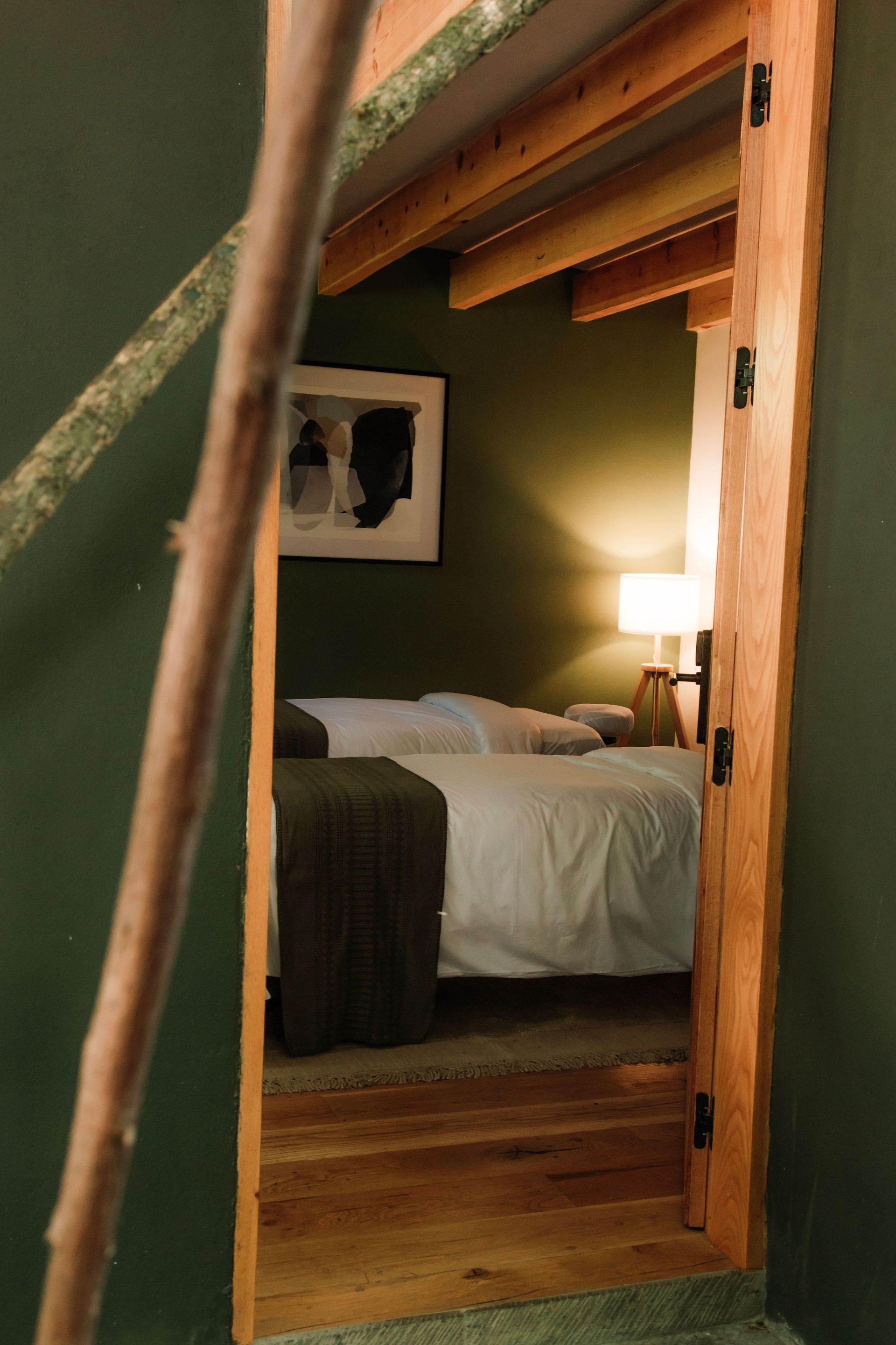 Cabina de masaje  vista a través de una puerta, con una cama, luz cálida de una lámpara y vigas de madera en el techo.