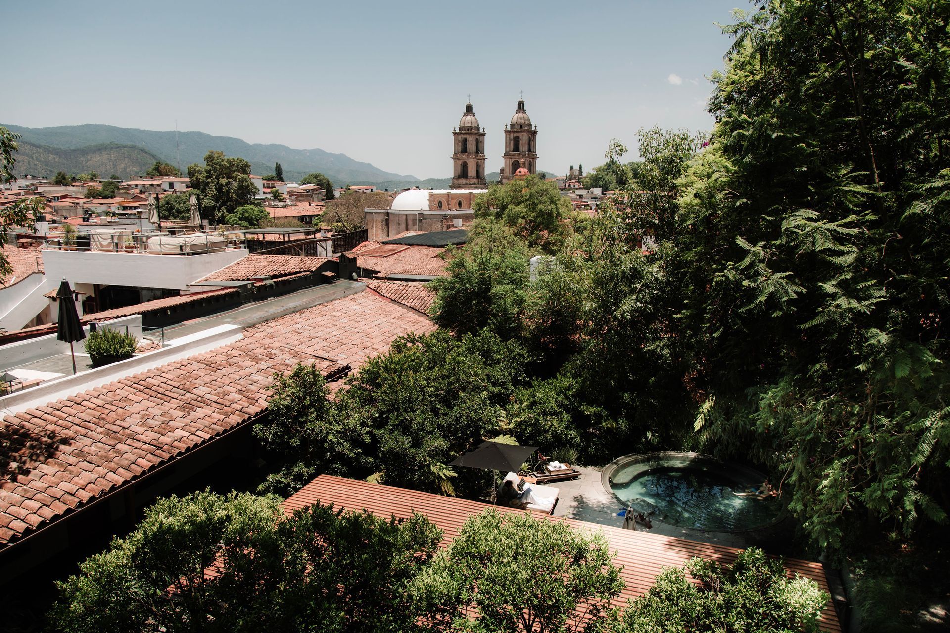 Tejados y árboles en un valle soleado, con dos torres de iglesia gemelas en la distancia.