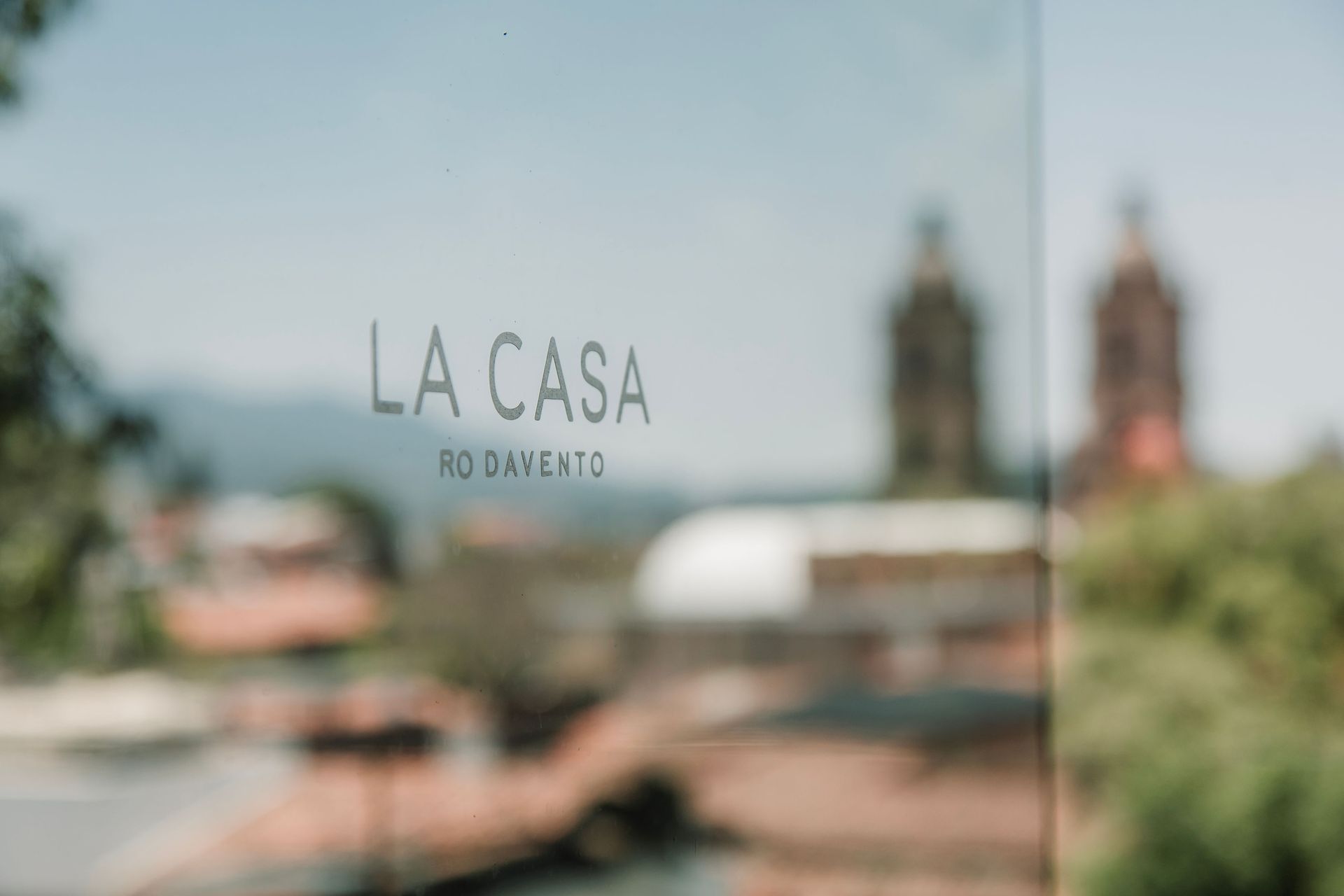 Vista borrosa del exterior del letrero del restaurante La Casa con las torres de la iglesia al fondo.