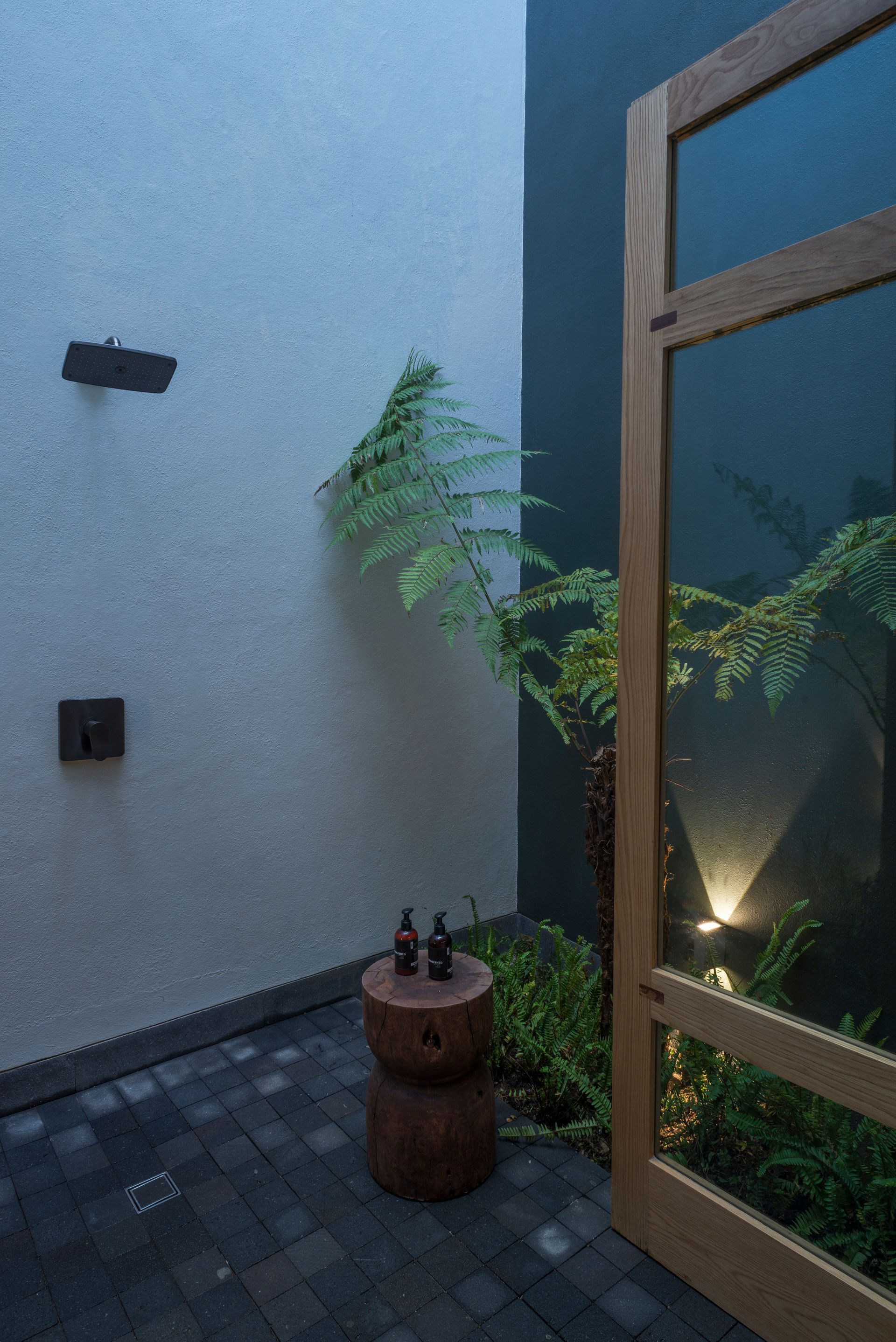 Precioso outdoor shower con puertas de madera.y cristal, rodeado de plantas y luz natural
