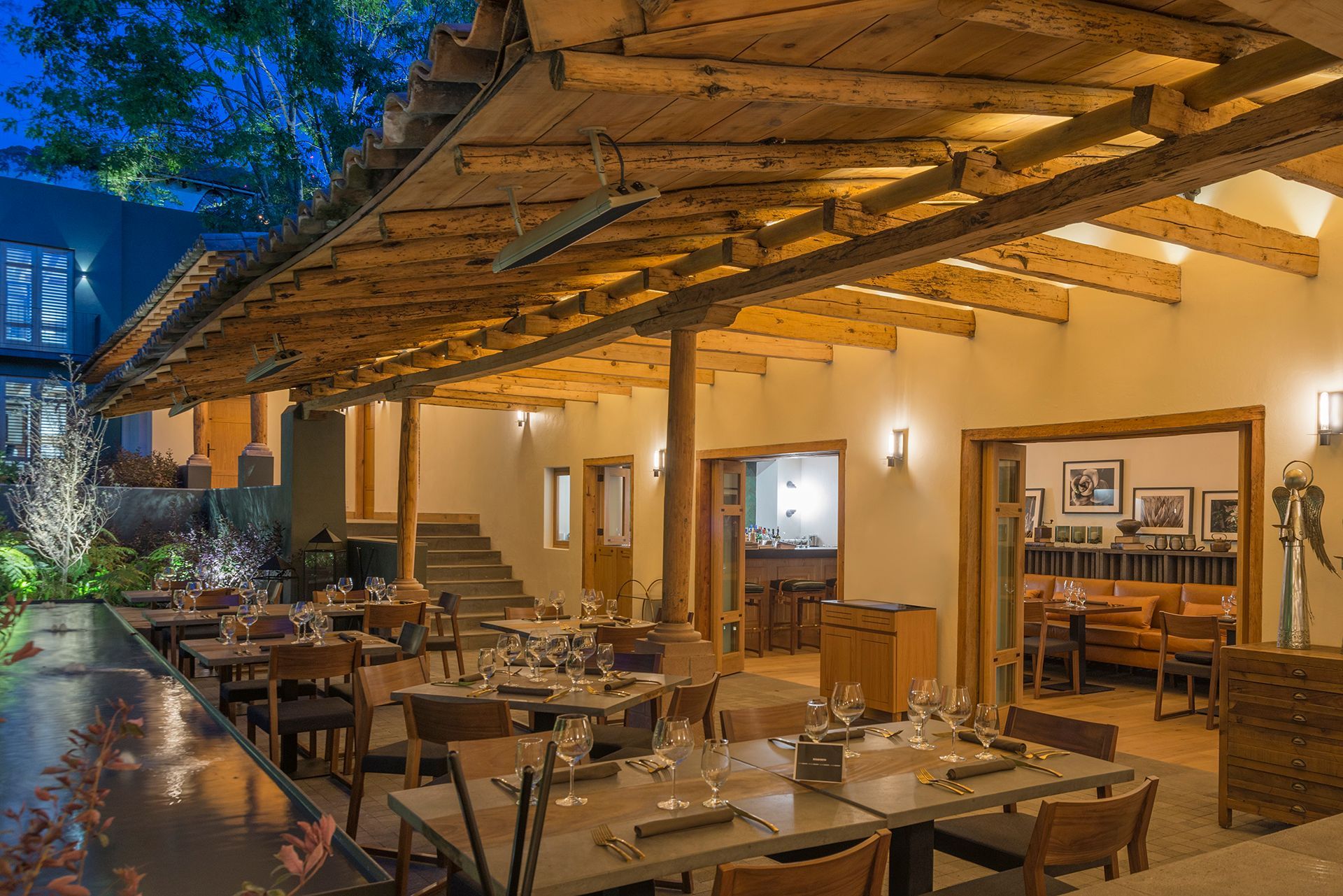 Terraza de restaurante al aire libre con mesas de madera, iluminación cálida y techo de paja al atardecer.