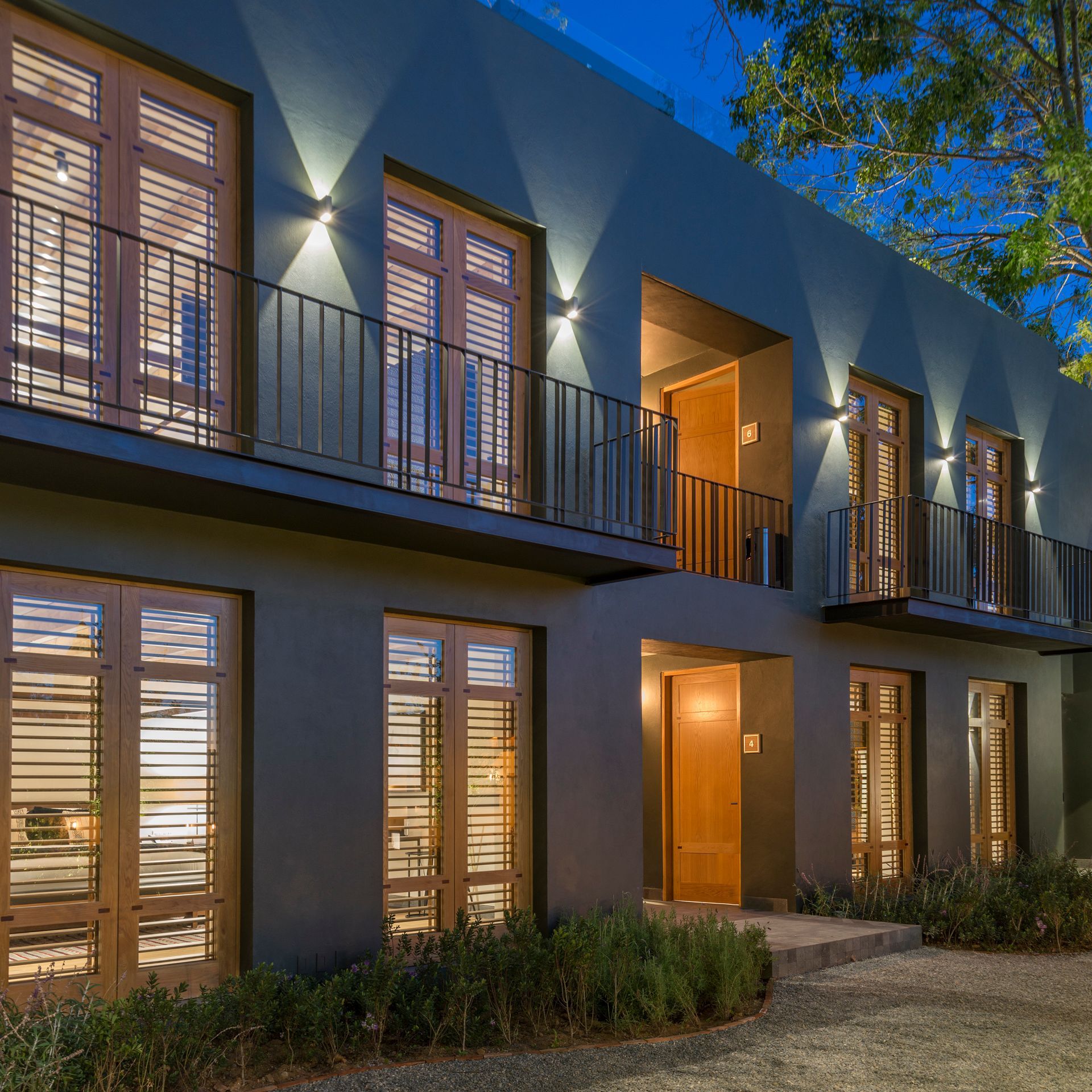 Exterior de una casa moderna de dos plantas al anochecer, con ventanas, balcón y porche delantero iluminados.