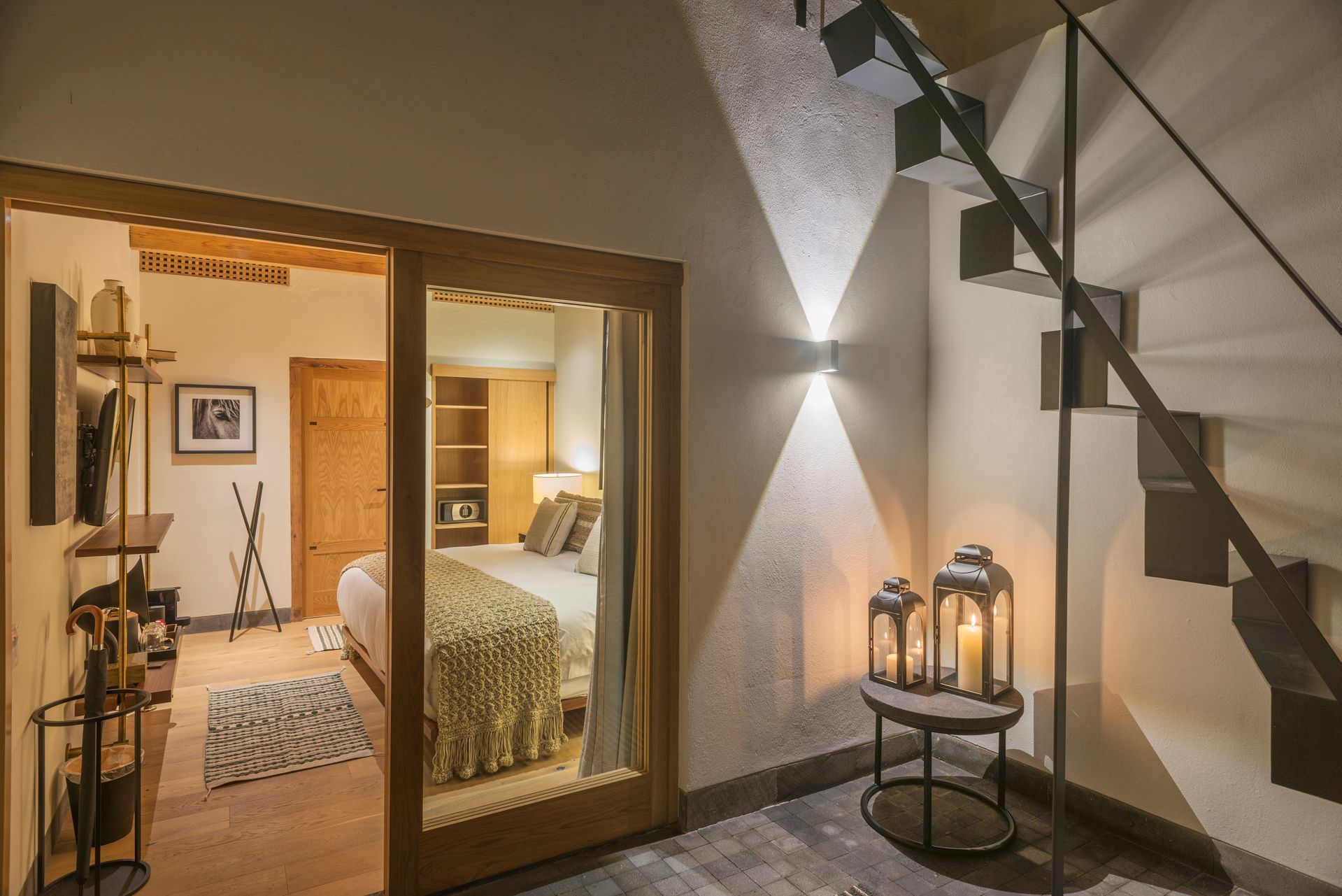 Acogedora habitación con vistas a través de puertas de cristal, escalera y faroles sobre una mesita.