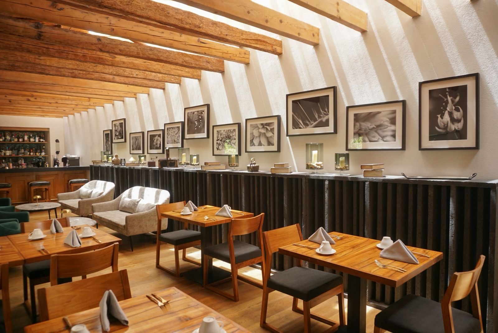 Elegante comedor de restaurante con vigas de madera, cuadros enmarcados, sillas blancas y mesas puestas.