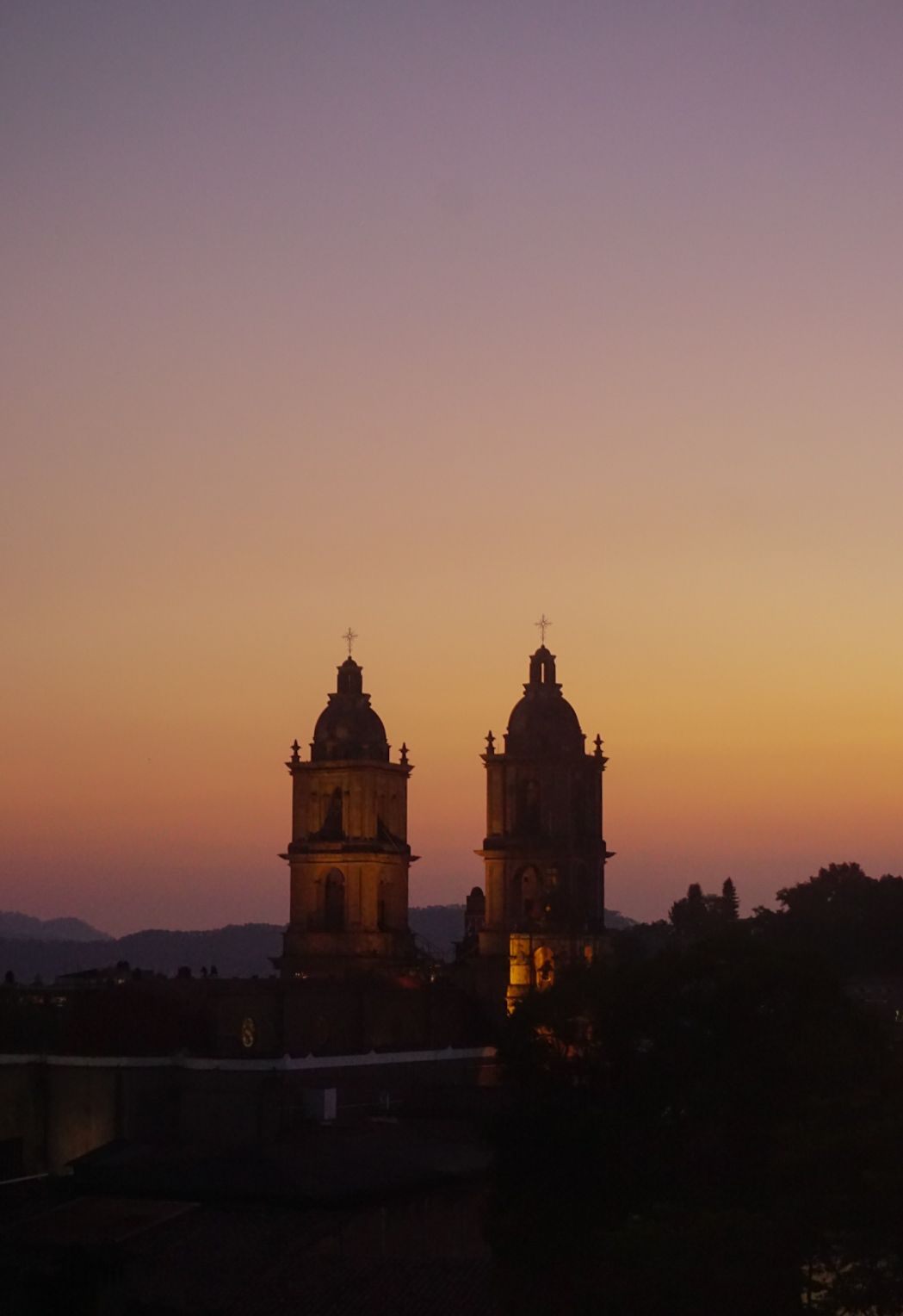 Puesta de sol sobre dos torres de iglesia recortadas contra un cielo rosa anaranjado.