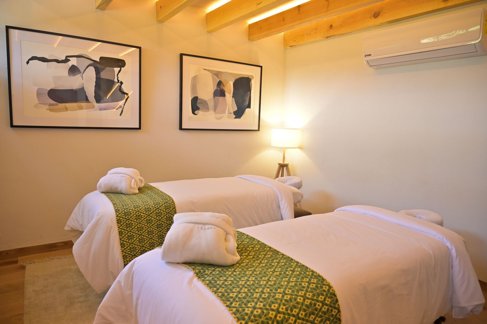 Cabina de masaje para parejas, decorada con pie de cama verde y cuadros blanco y negro, espacio acogedor y cálido.