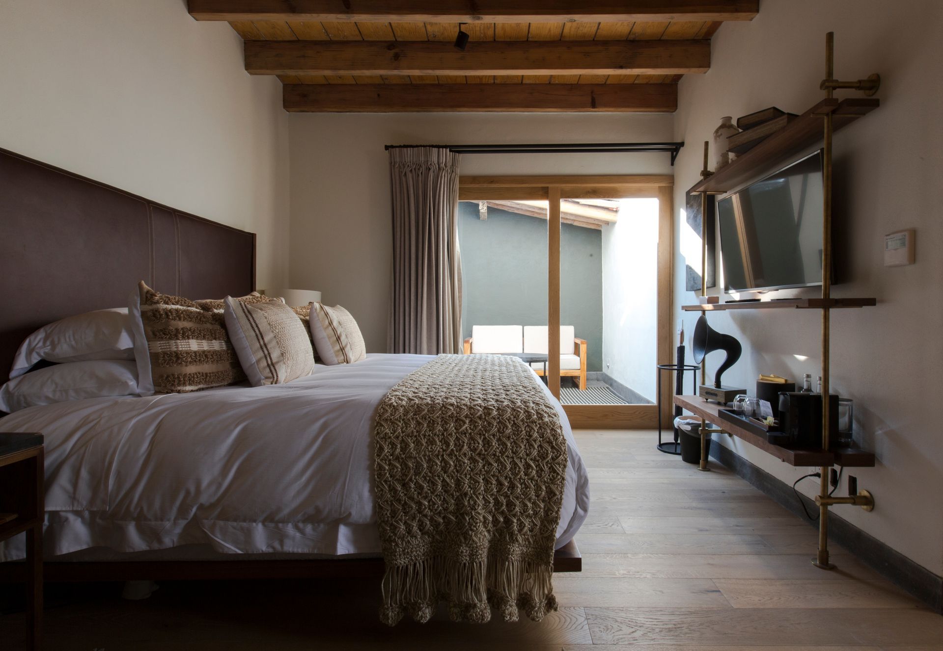 Habitación acogedora con una cama grande, vigas de madera y vistas al balcón a través de puertas corredizas de cristal.