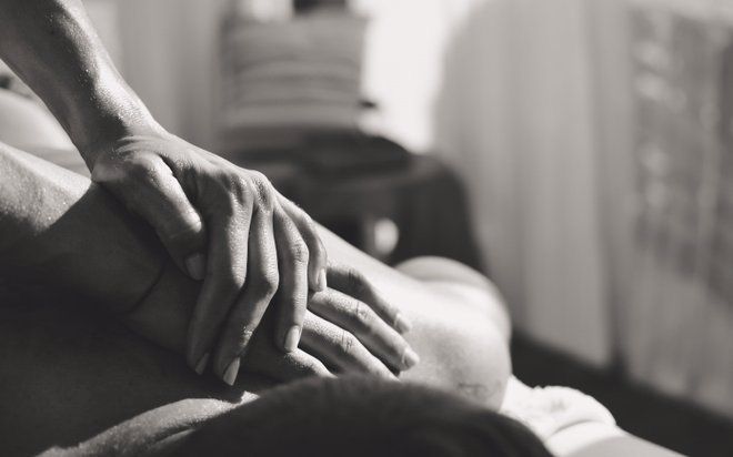 Manos que descansan suavemente sobre la espalda de una persona durante un masaje en una habitación con iluminación tenue.