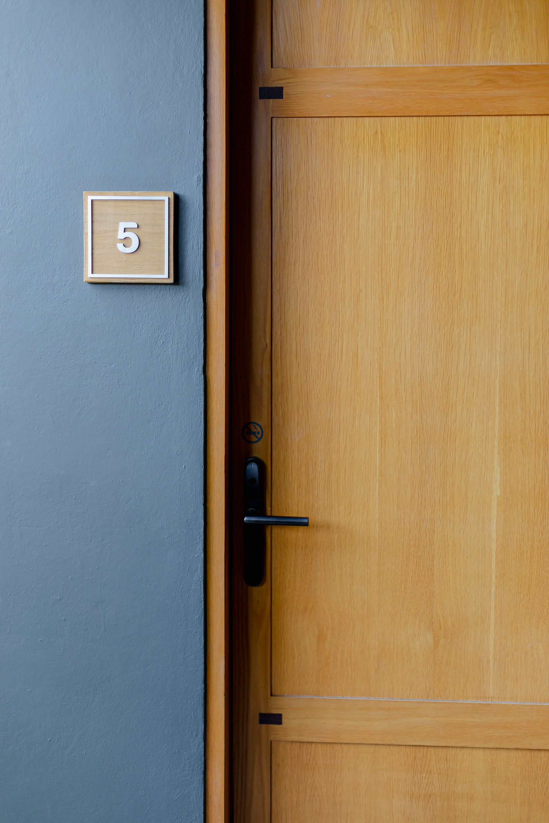 Puerta de madera junto a una pared azul con una pequeña placa cuadrada con el número 5.