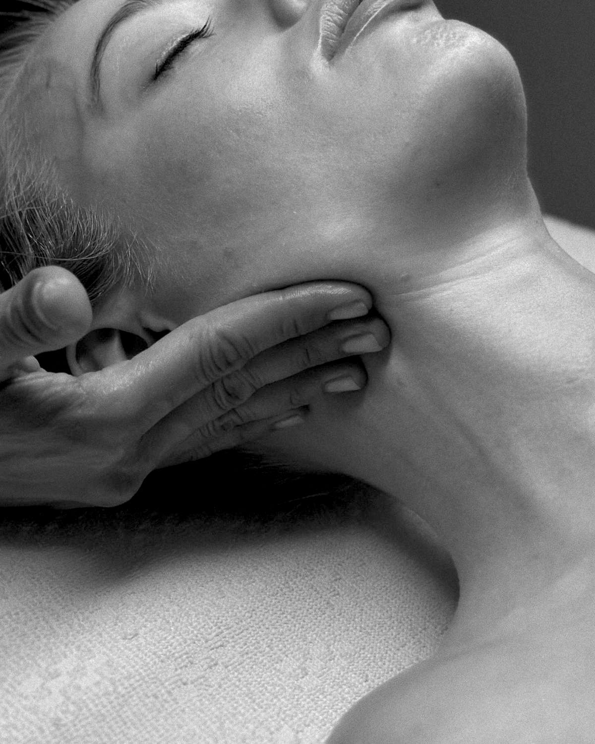 Primer plano del cuello de una persona al que otra mano le da un suave masaje, en blanco y negro.