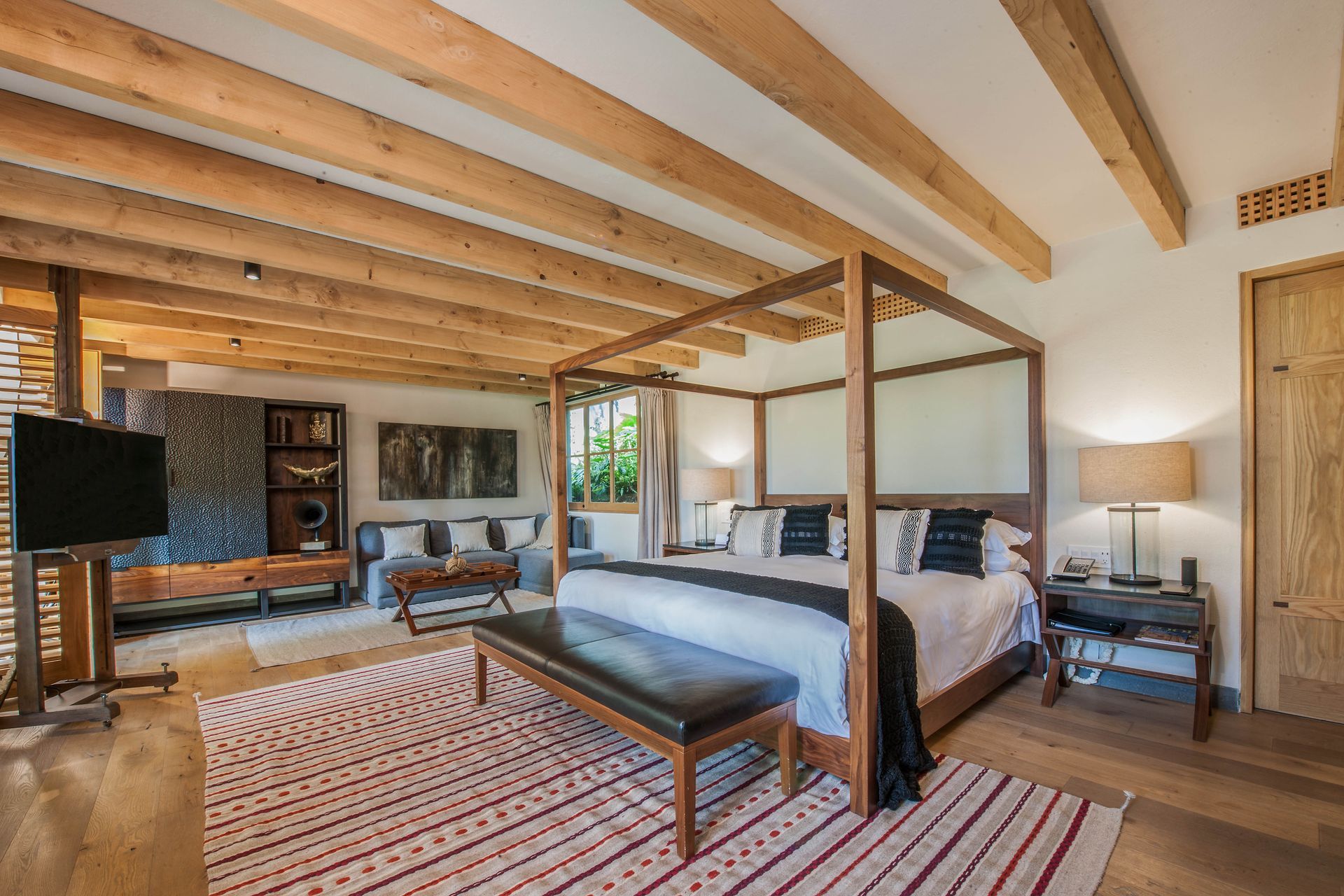 Amplia habitación rústica con vigas de madera, cama con dosel, alfombras a rayas, televisor y zona de estar.