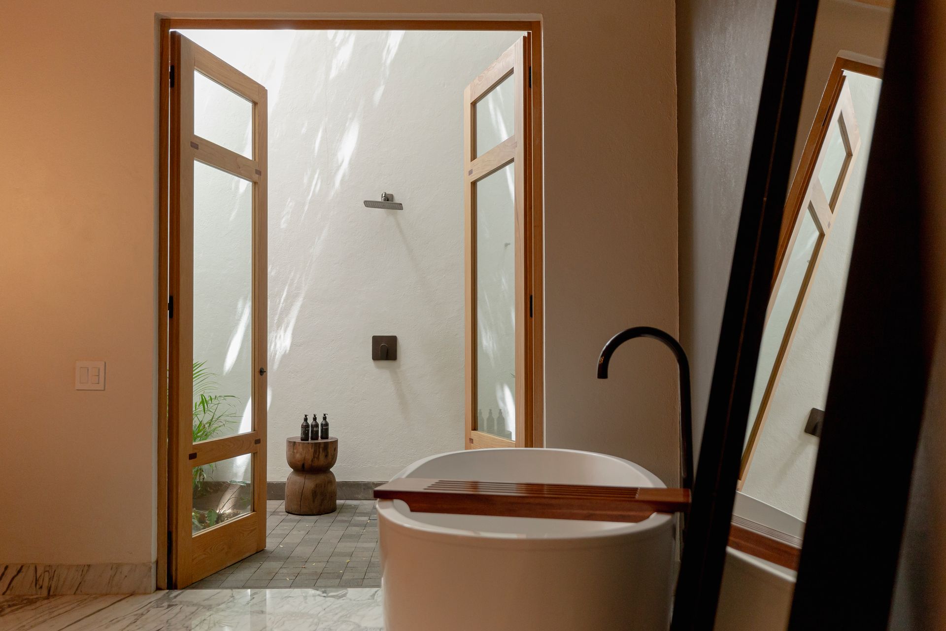 Baño moderno con bañera independiente, puertas de cristal abiertas y una ducha a ras de suelo.