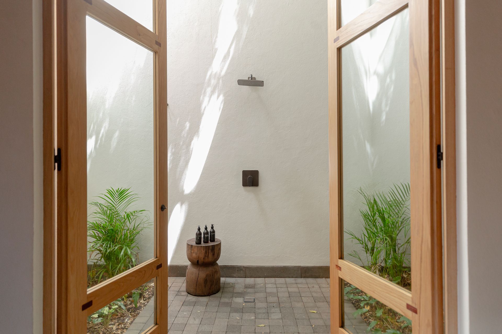 Precioso outdoor shower con puertas de madera.y cristal, rodeado de plantas y luz natural
