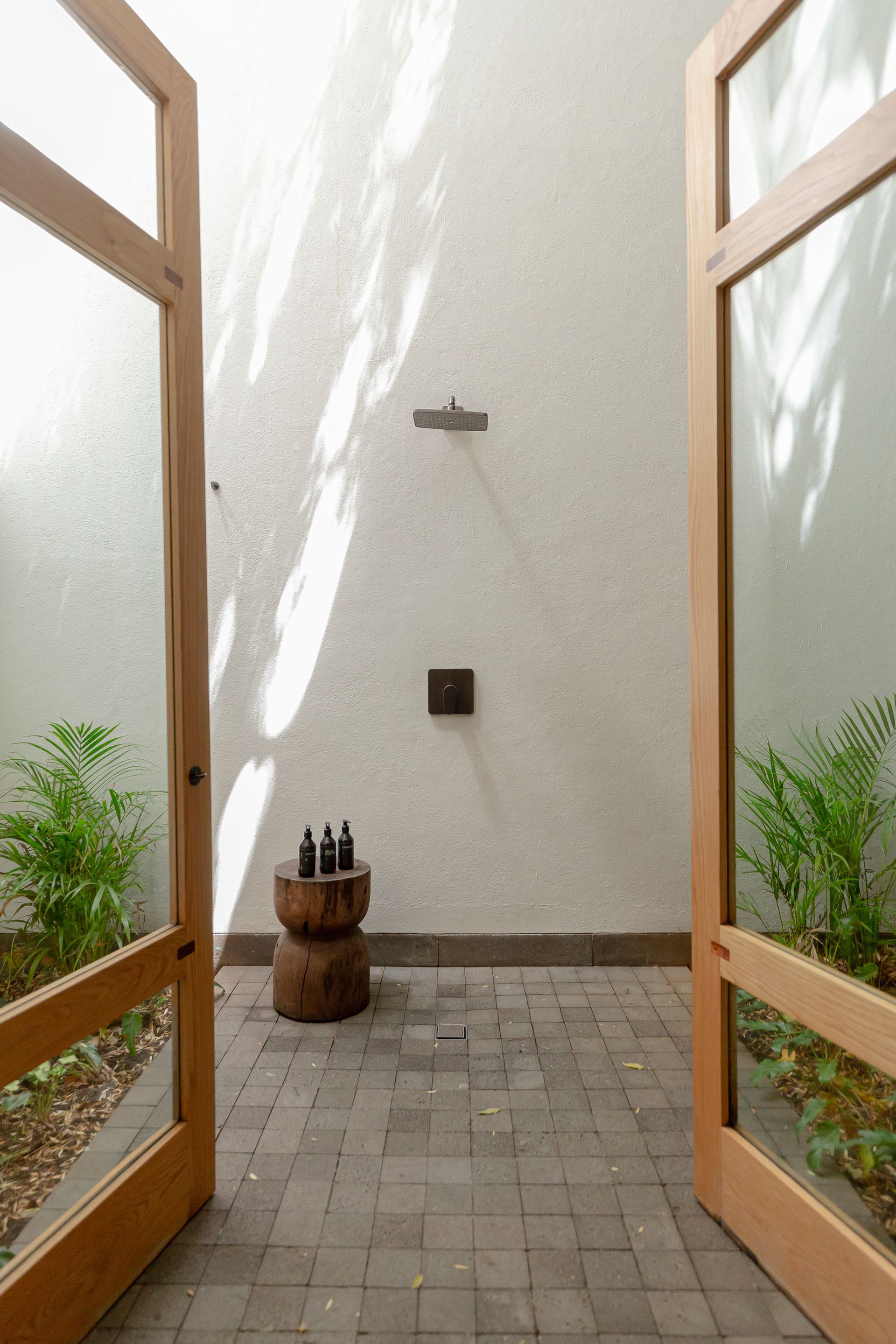 Entrada al patio con puertas de madera abiertas, plantas en macetas y un pequeño taburete sobre un suelo de baldosas.
