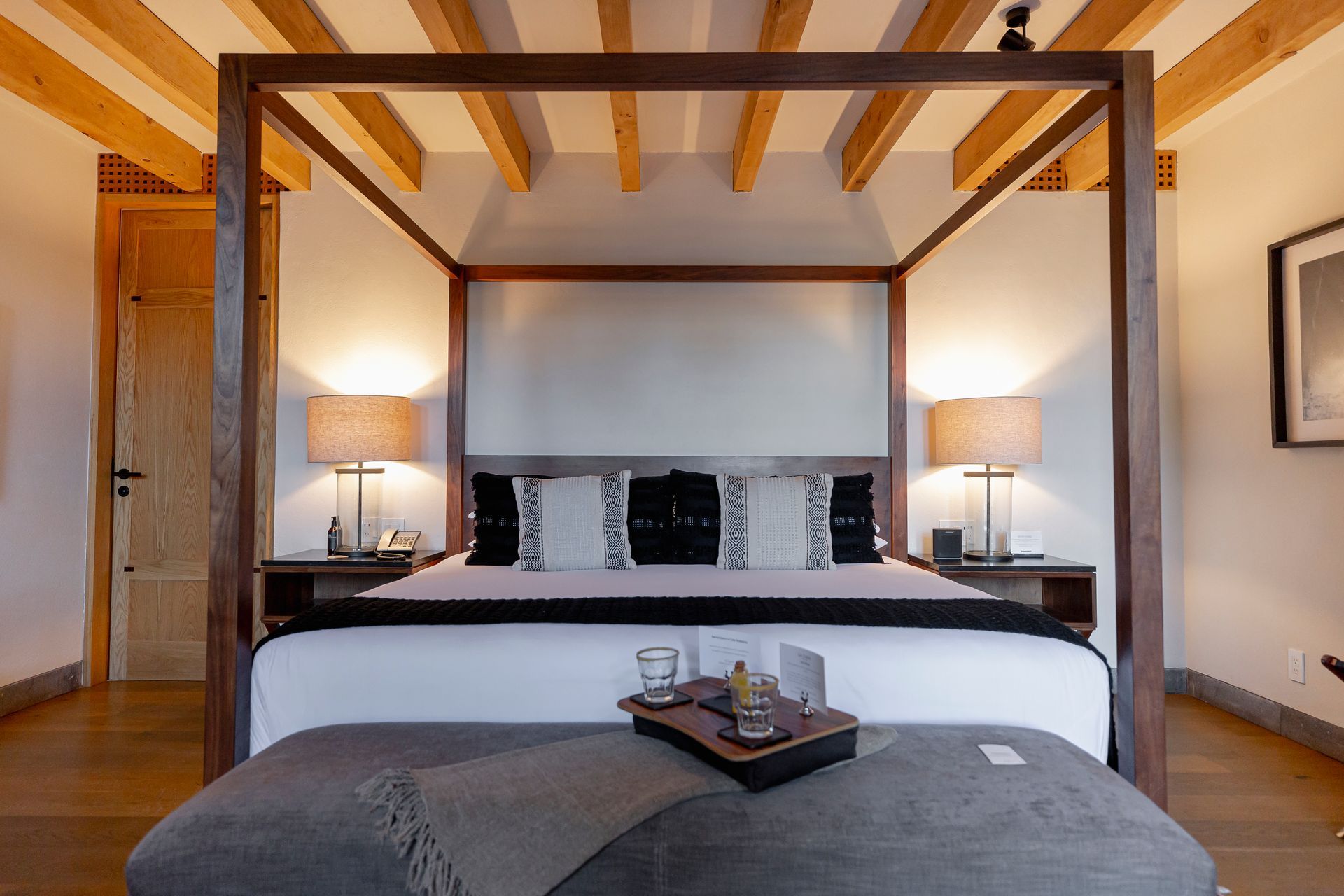 Dormitorio moderno con cama con dosel, lámparas de noche y una bandeja a los pies de la cama.