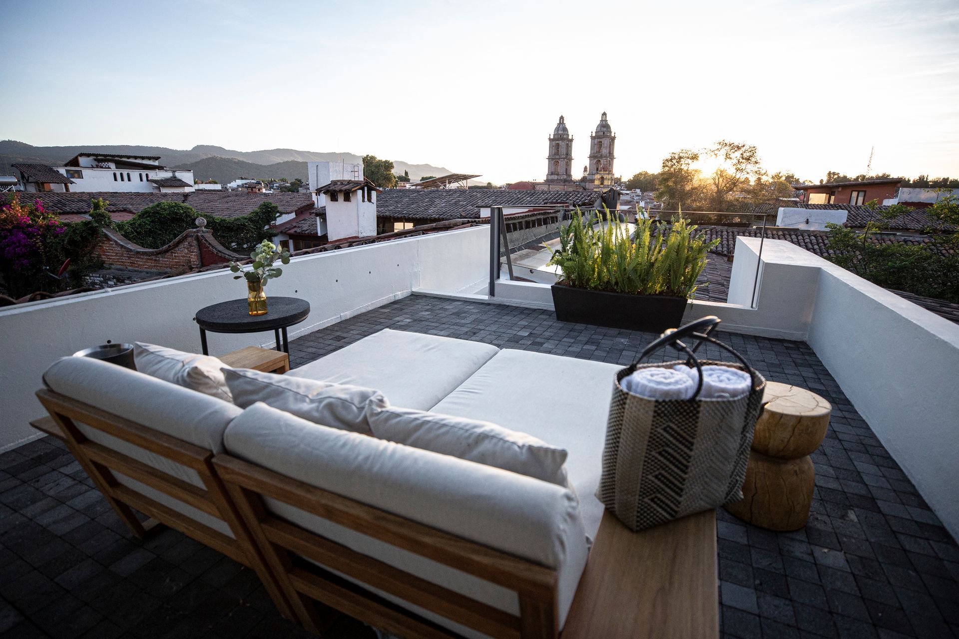 Rooftop con camastro de madera y tela blanca, vegetación y vistas a la catedral y el centro de Valle de Bravo al atardecer.