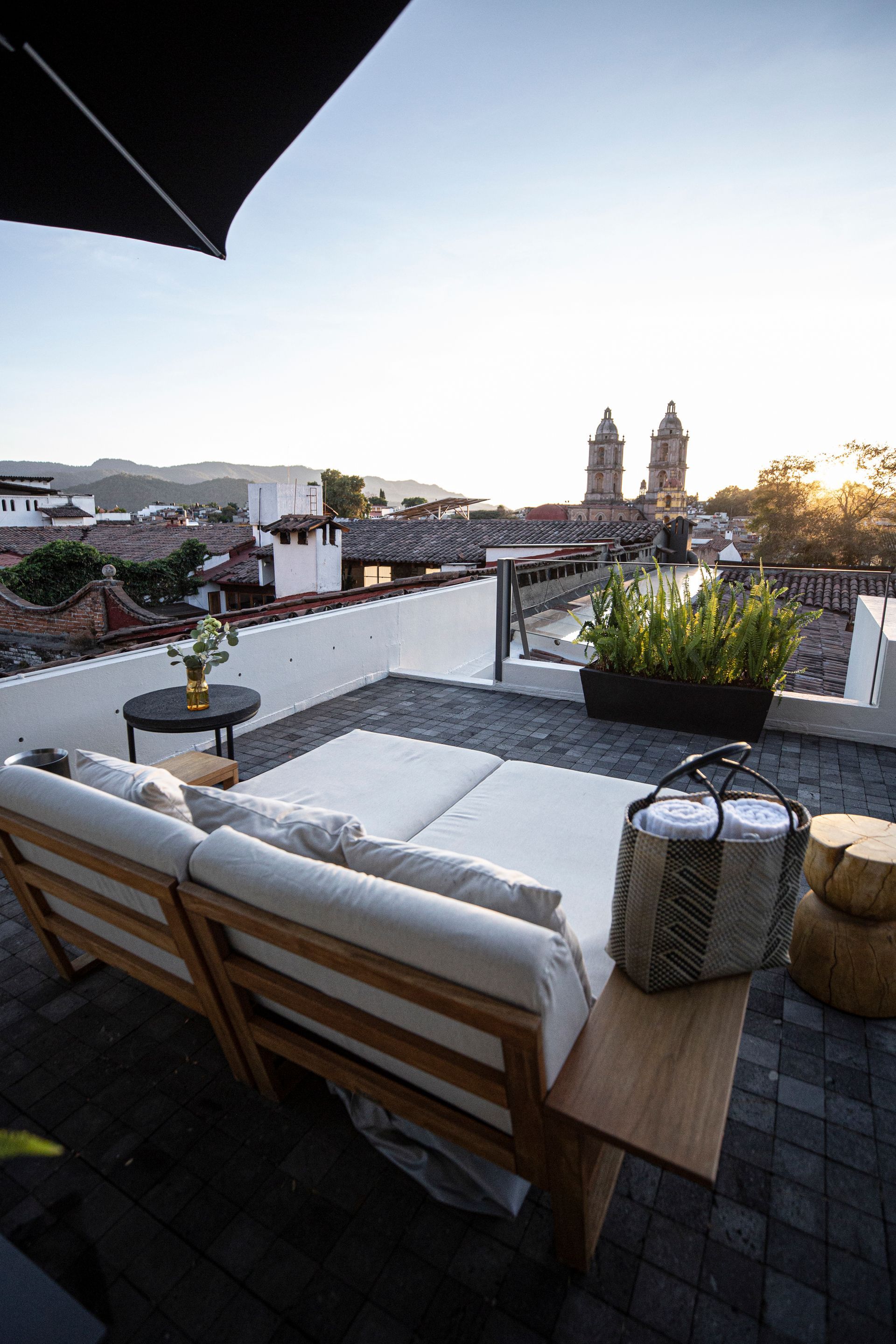 Terraza en la azotea con sillones blancos, plantas en macetas y vistas a la ciudad al atardecer.
