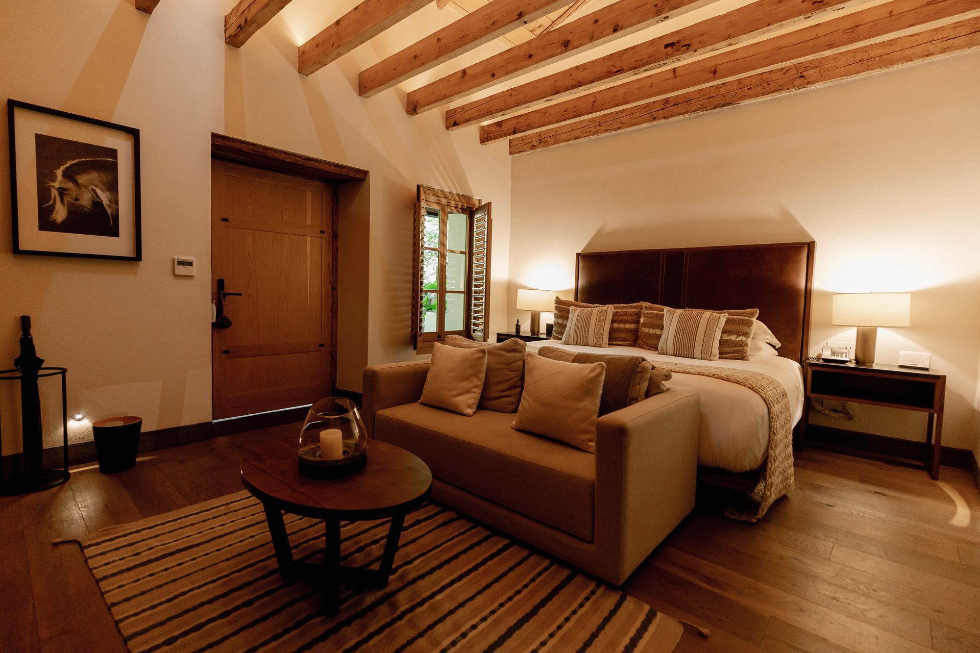 Habitación acogedora con sofá a los pies de la cama, iluminación cálida, vigas de madera y una puerta rústica de madera.