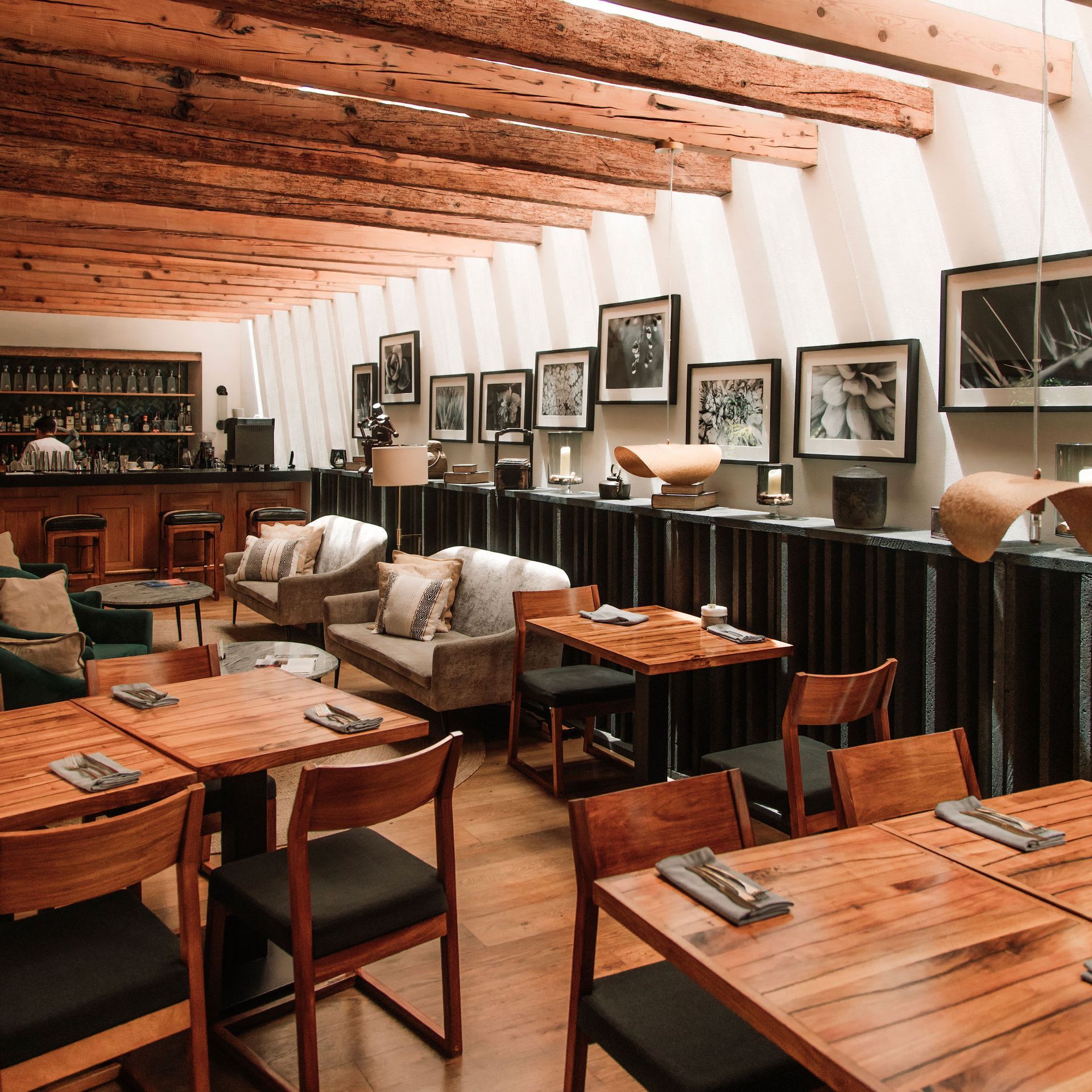 Interior cálido del restaurante revestido de madera con mesas, sillas, cuadros y una barra a lo largo de la pared.