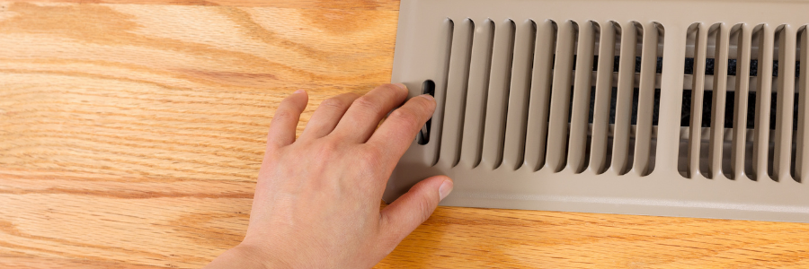 A person is touching a vent on a wooden floor.
