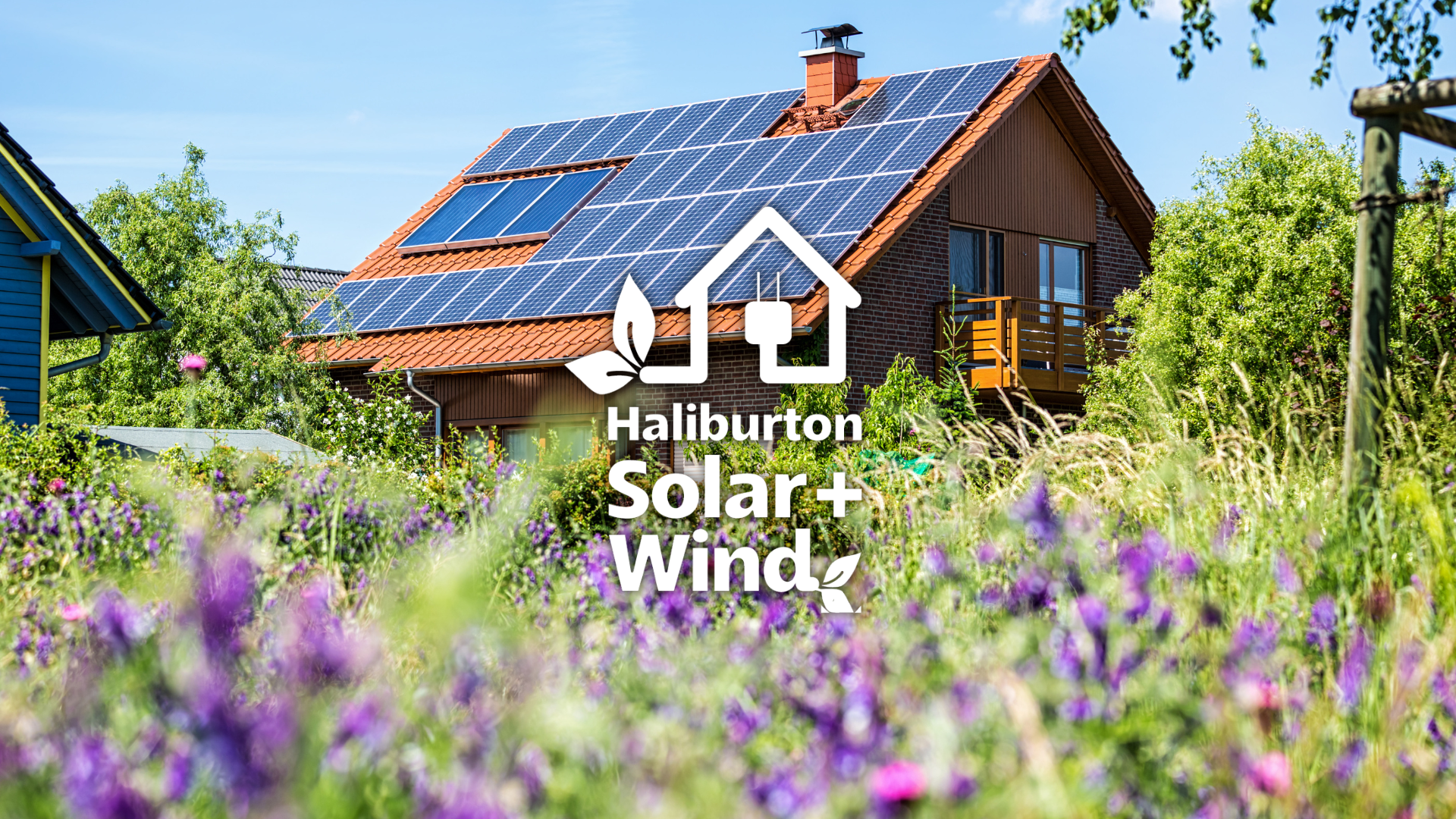A house with solar panels on the roof is surrounded by purple flowers.
