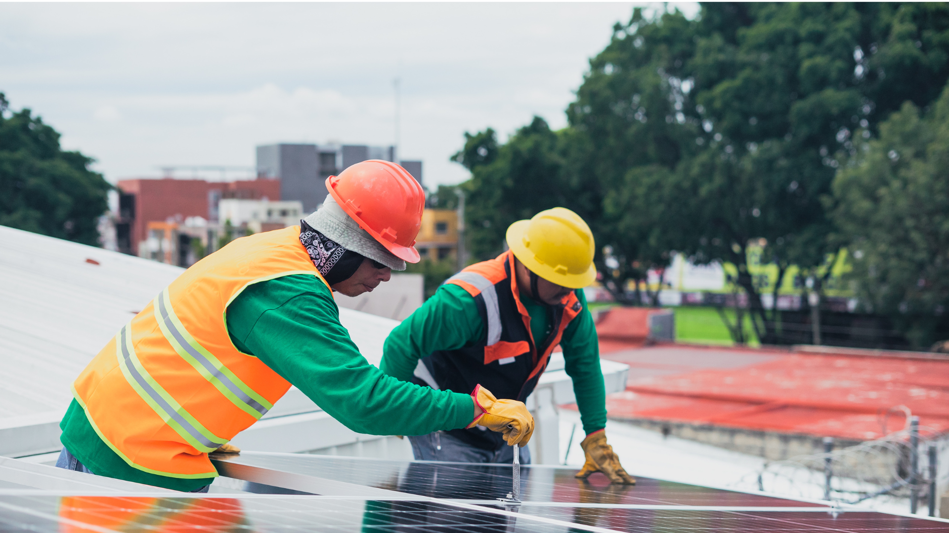 Two workers in hard hats install solar panels on a rooftop.