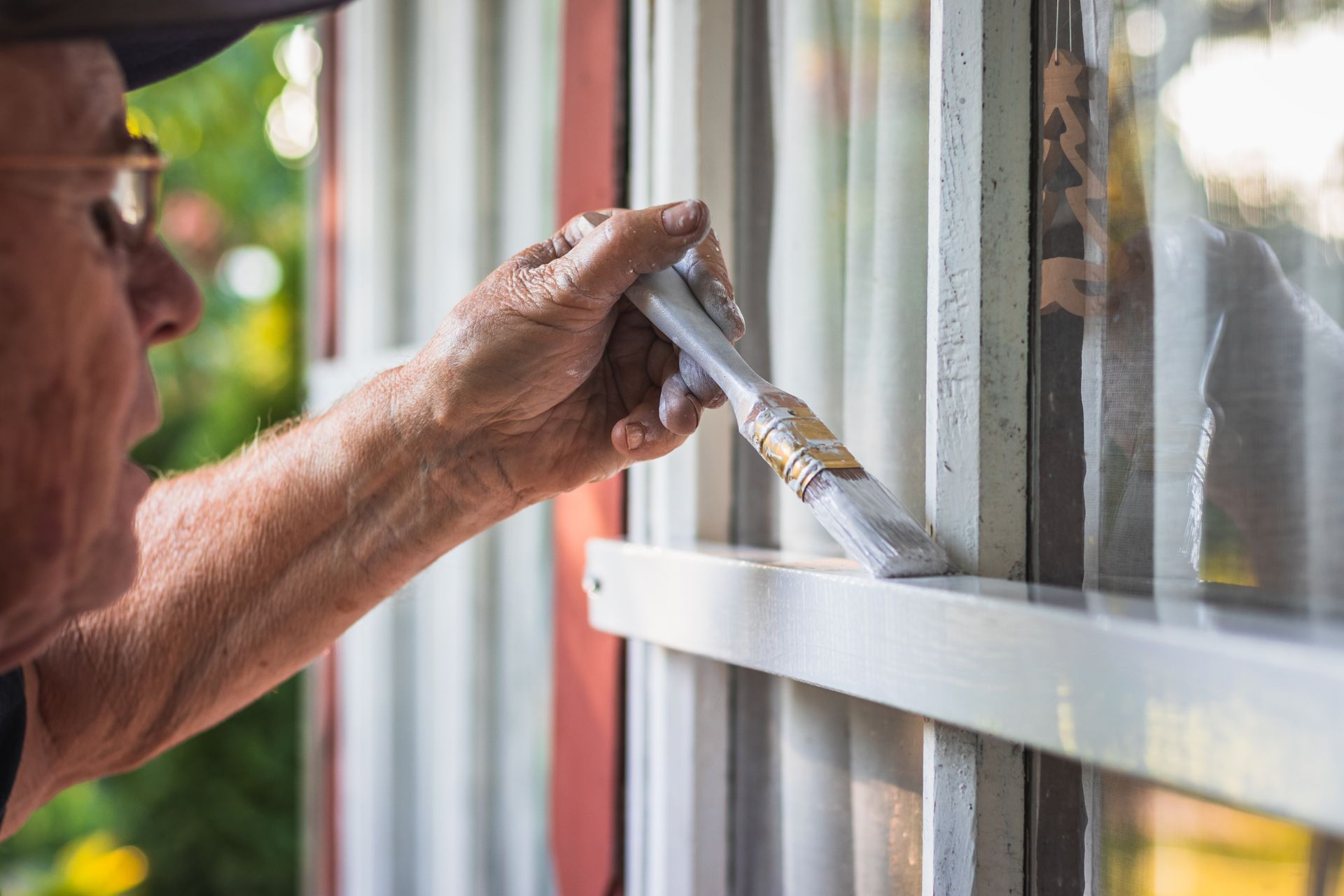 Hand applying white paint to a window frame with a brush