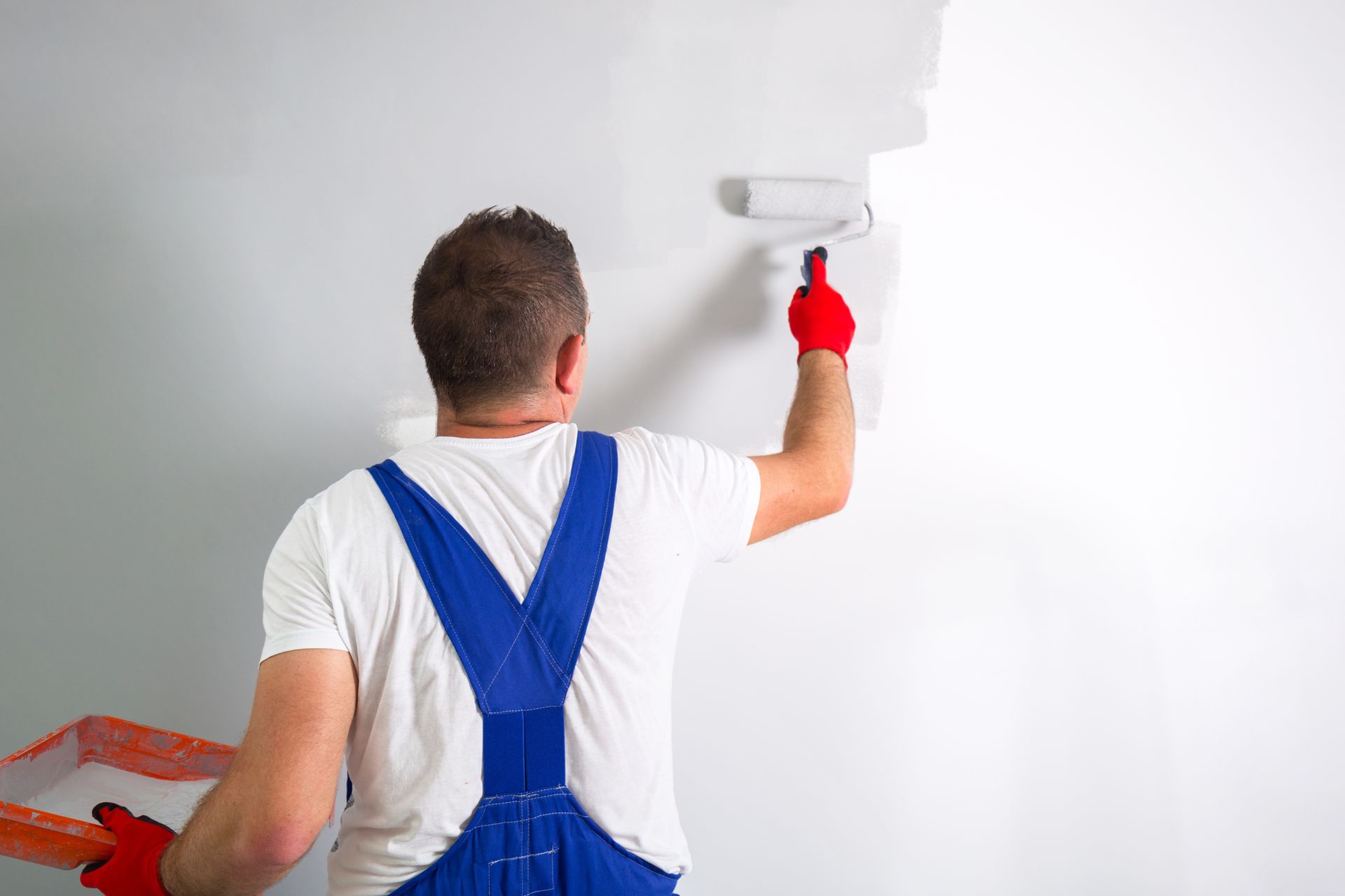 Painter using a red paint roller to paint a white wall