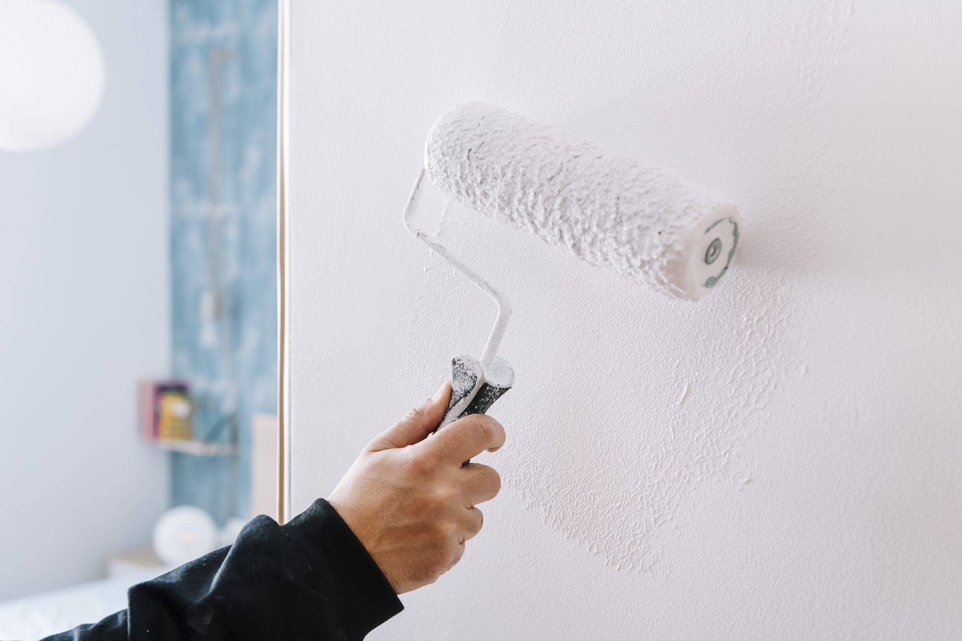 Person painting a white wall with a roller brush