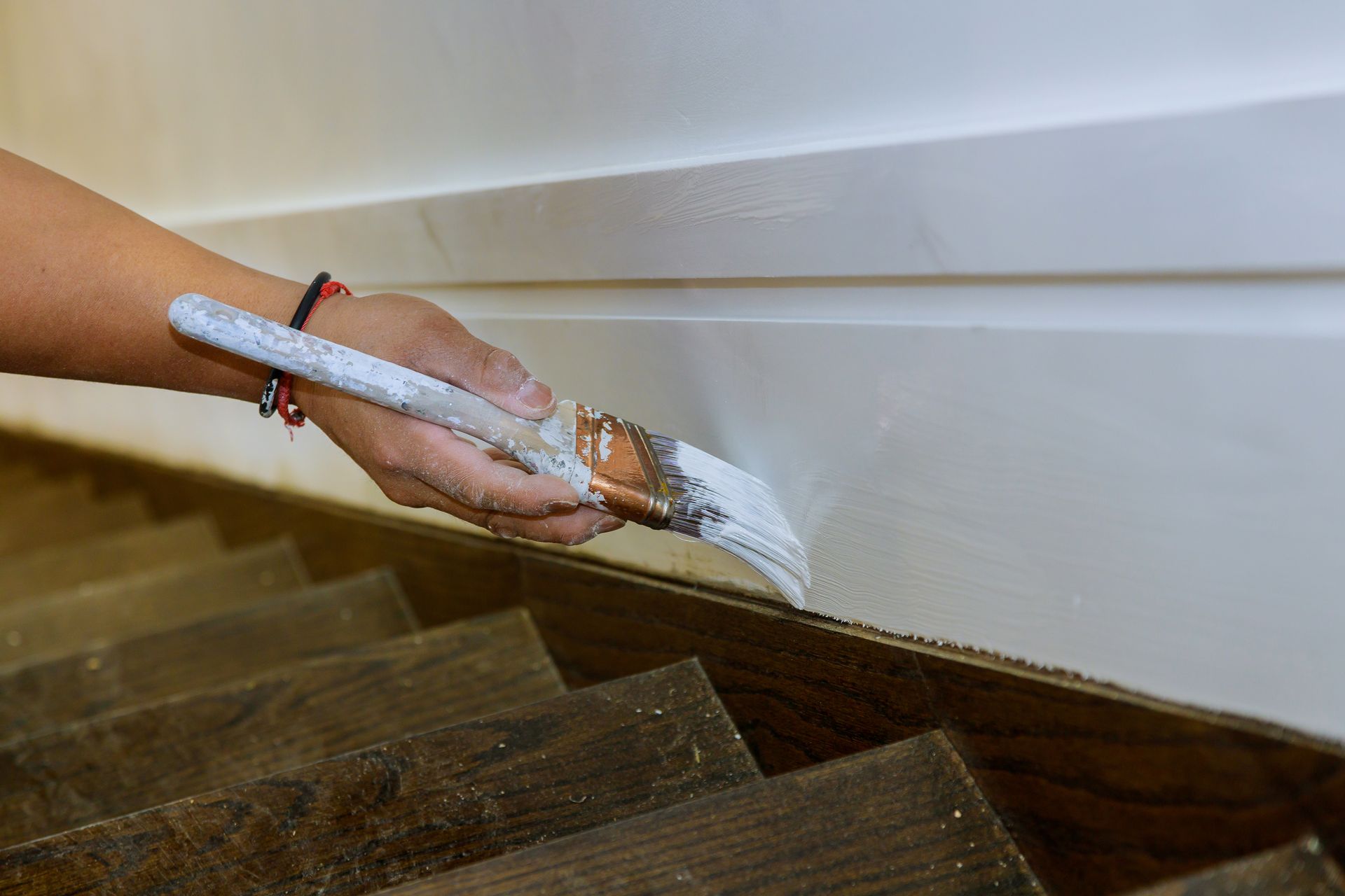 Hand painting a white stair trim with a small brush above dark wooden steps