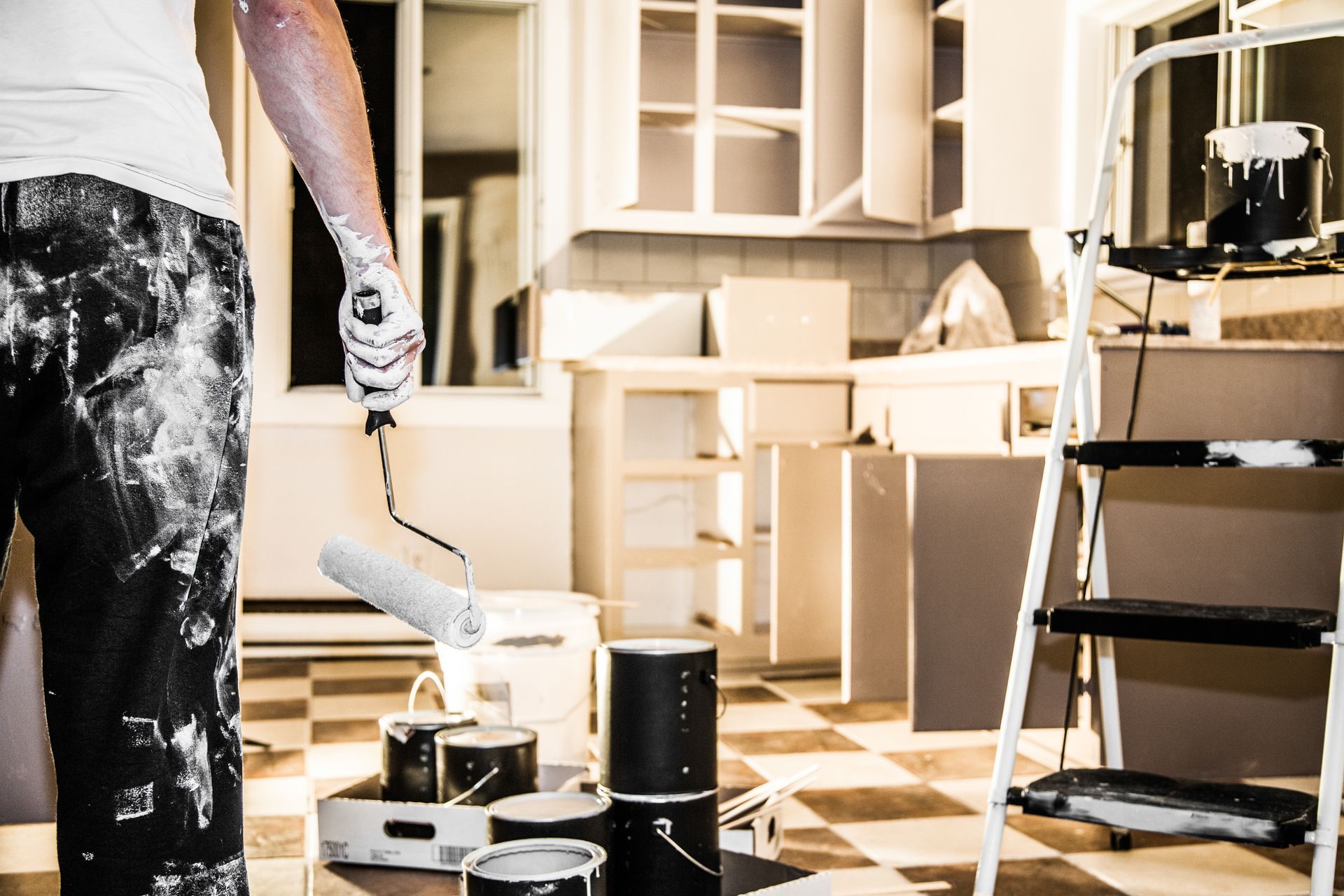 Person painting a room with a roller, surrounded by paint cans, shelves, and a ladder.