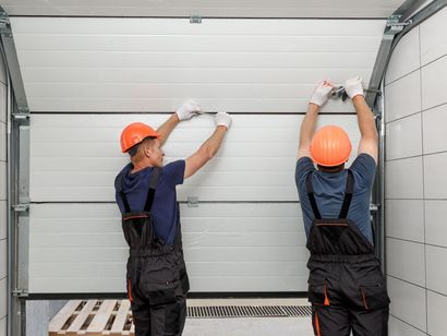 Deux hommes installent une porte de garage dans un garage.