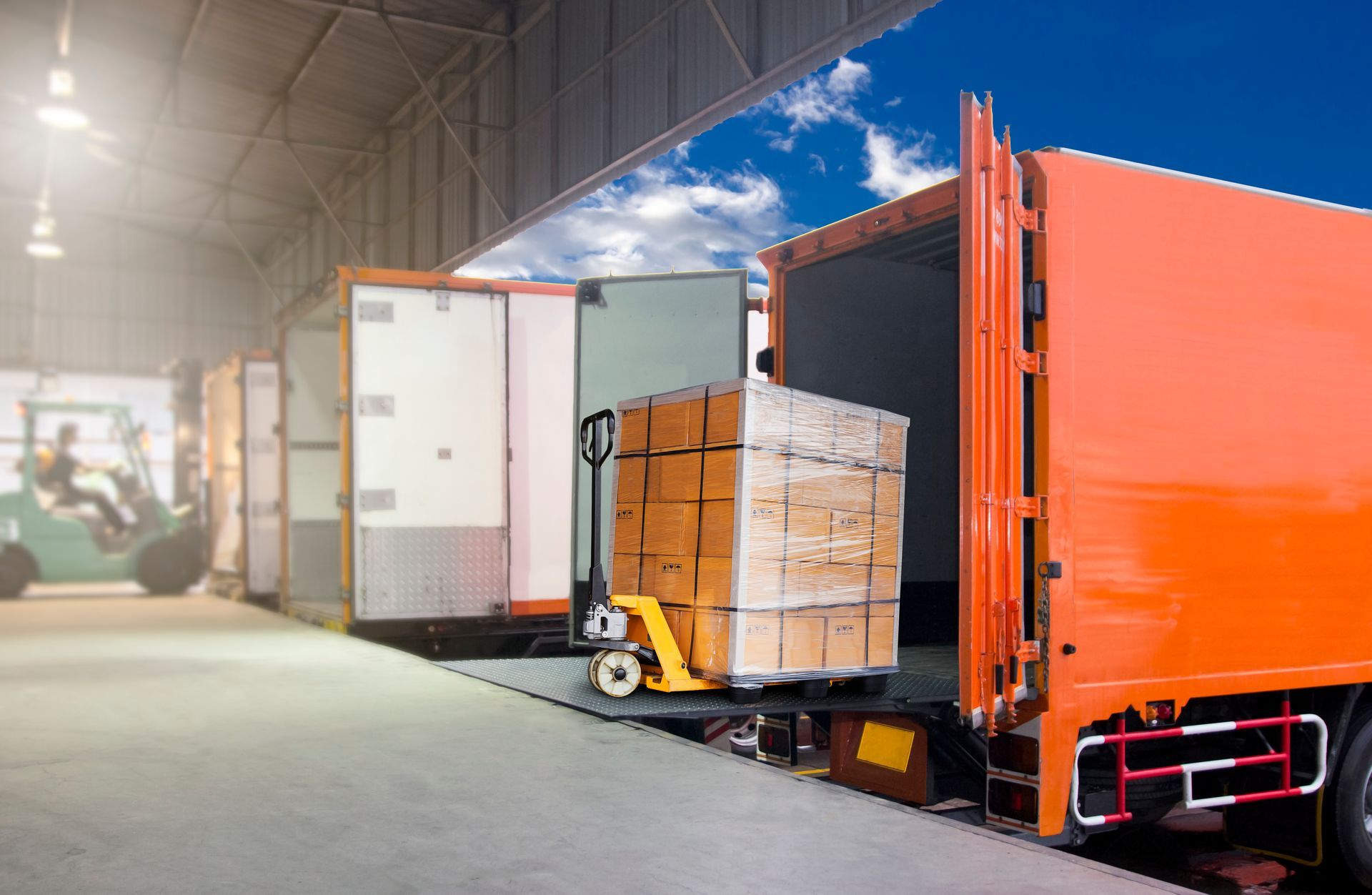 Une palette de cartons est chargée dans un camion orange depuis un quai de chargement.