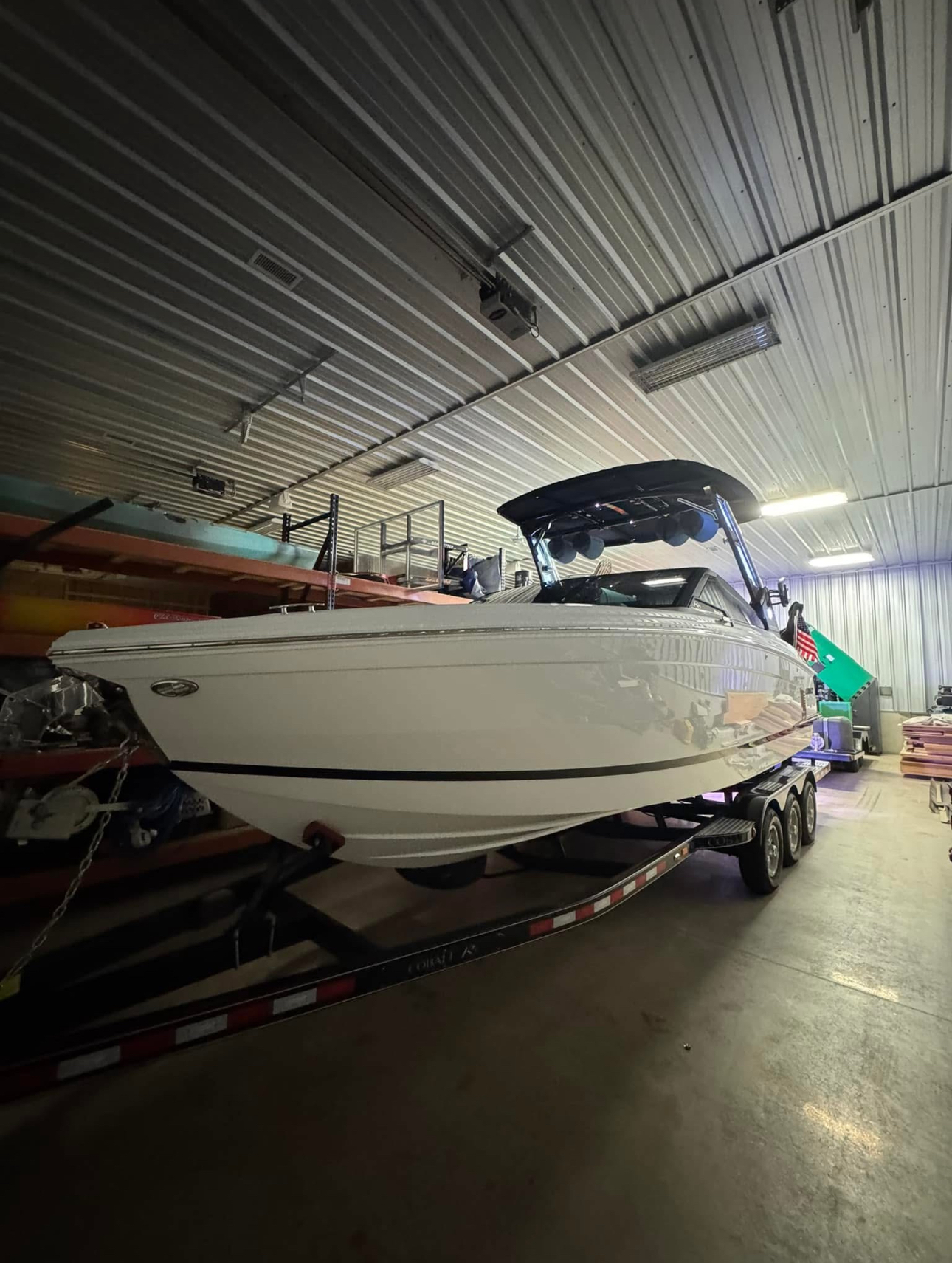 White motorboat on a trailer inside a building. Boat has a black canopy.