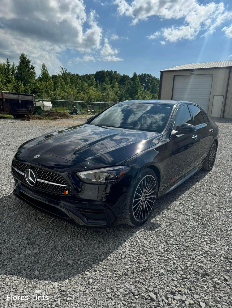 Black Mercedes sedan parked on gravel in front of a building on a sunny day.