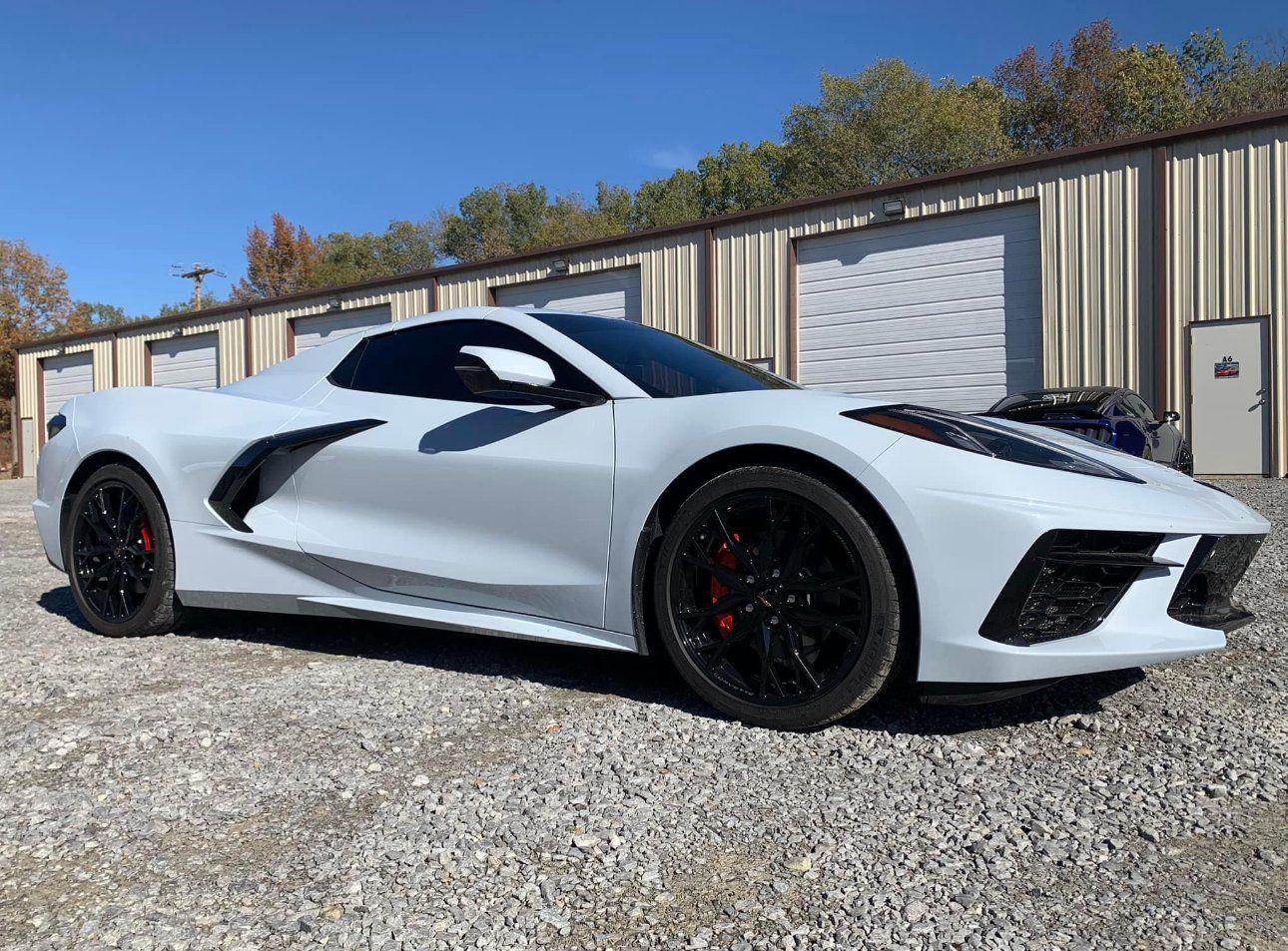 White sports car parked in front of a building with roll-up doors, sunny day.